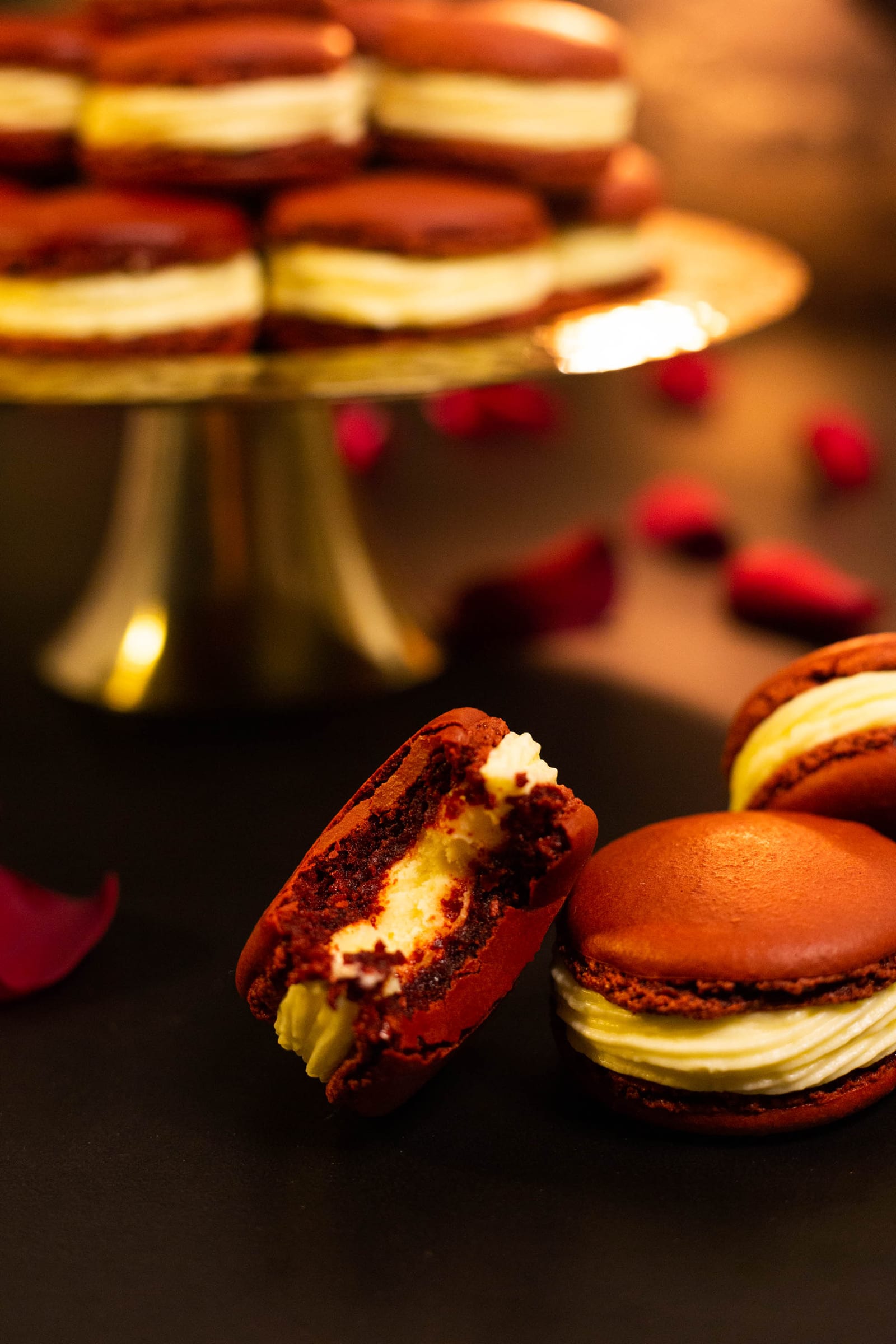 A bitten red velvet macaron showing its cheesecake disc and cream cheese frosting