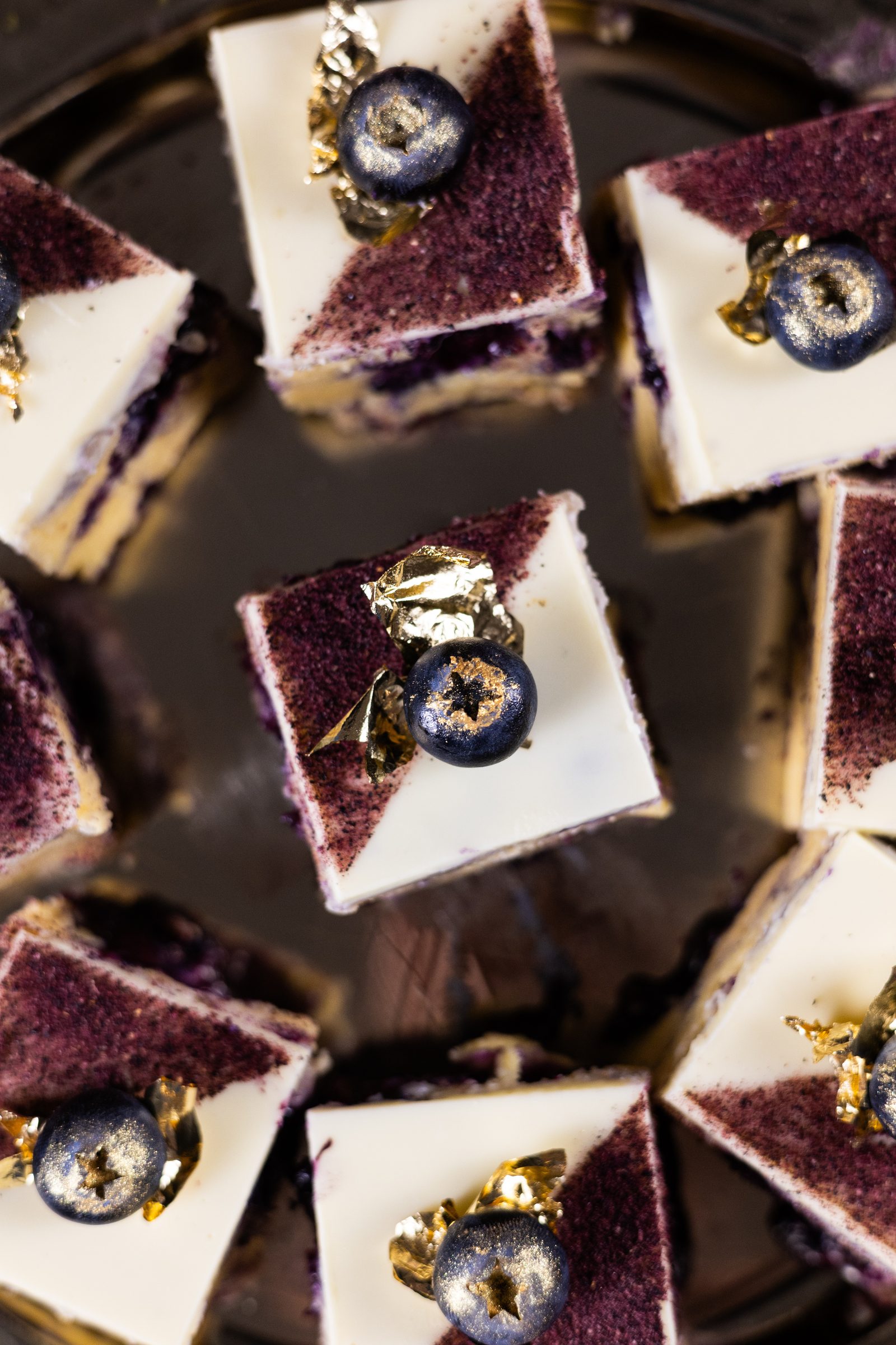 Close-up of blueberry ripple burfee squares with blueberries and gold leaf, from above