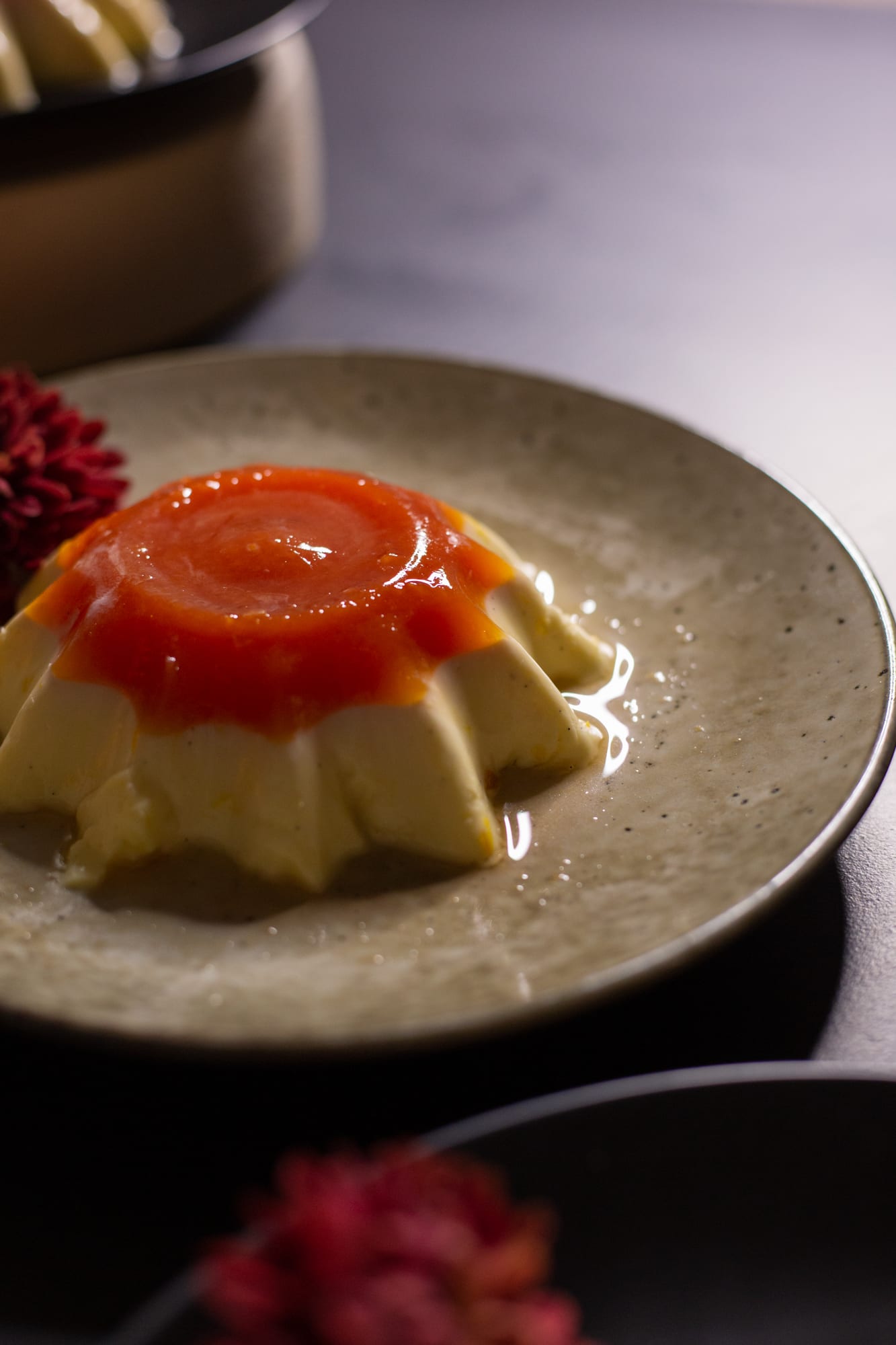 Close-up of the glossy blood orange jelly on a vanilla yoghurt panna cotta, a red flower in front