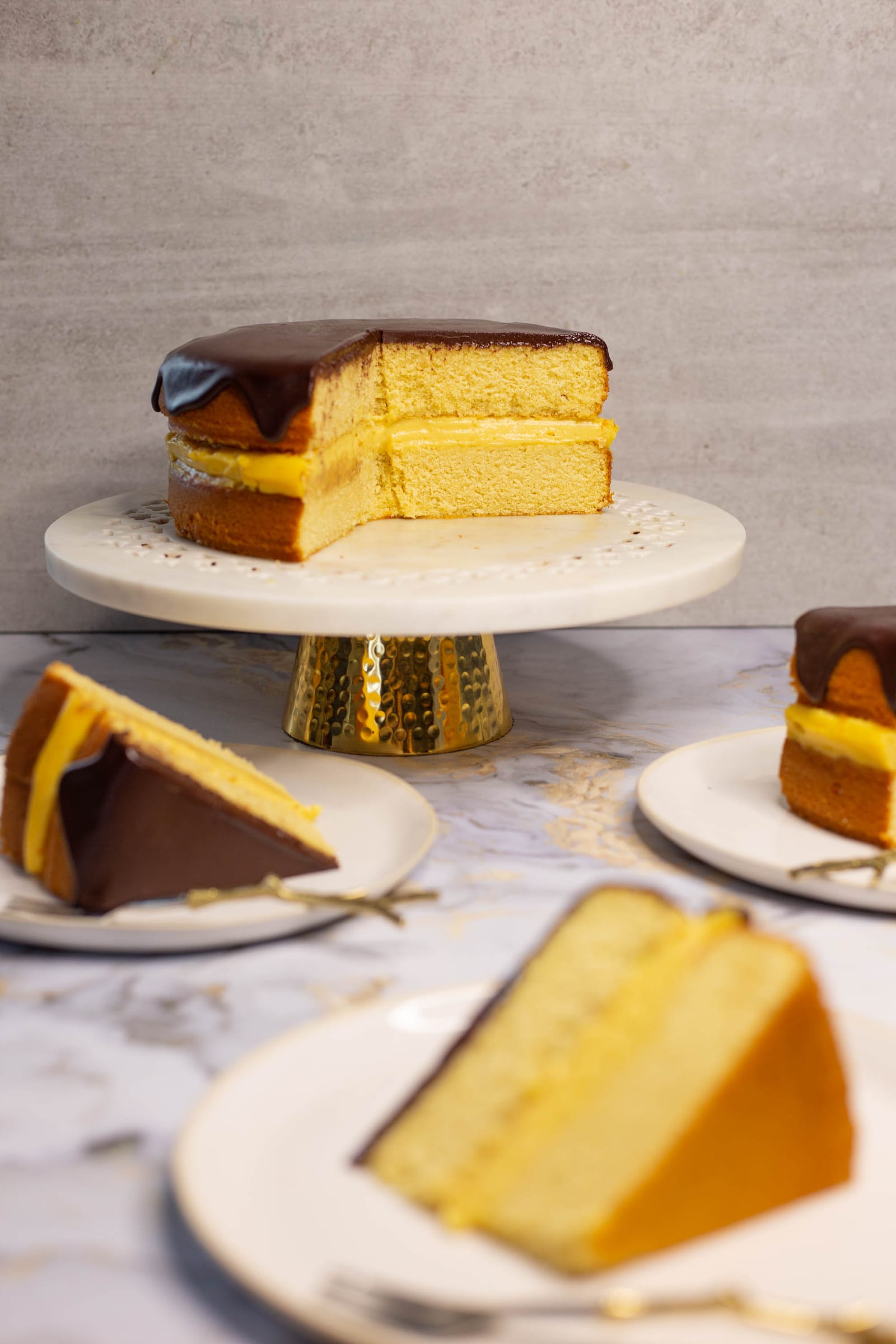 A Boston cream pie on its stand with slices served on plates in front