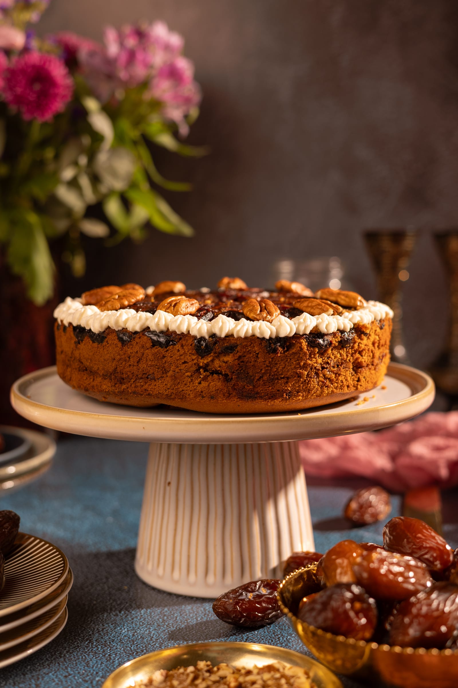The date and pecan cake on a white cake stand, with pink flowers and dates