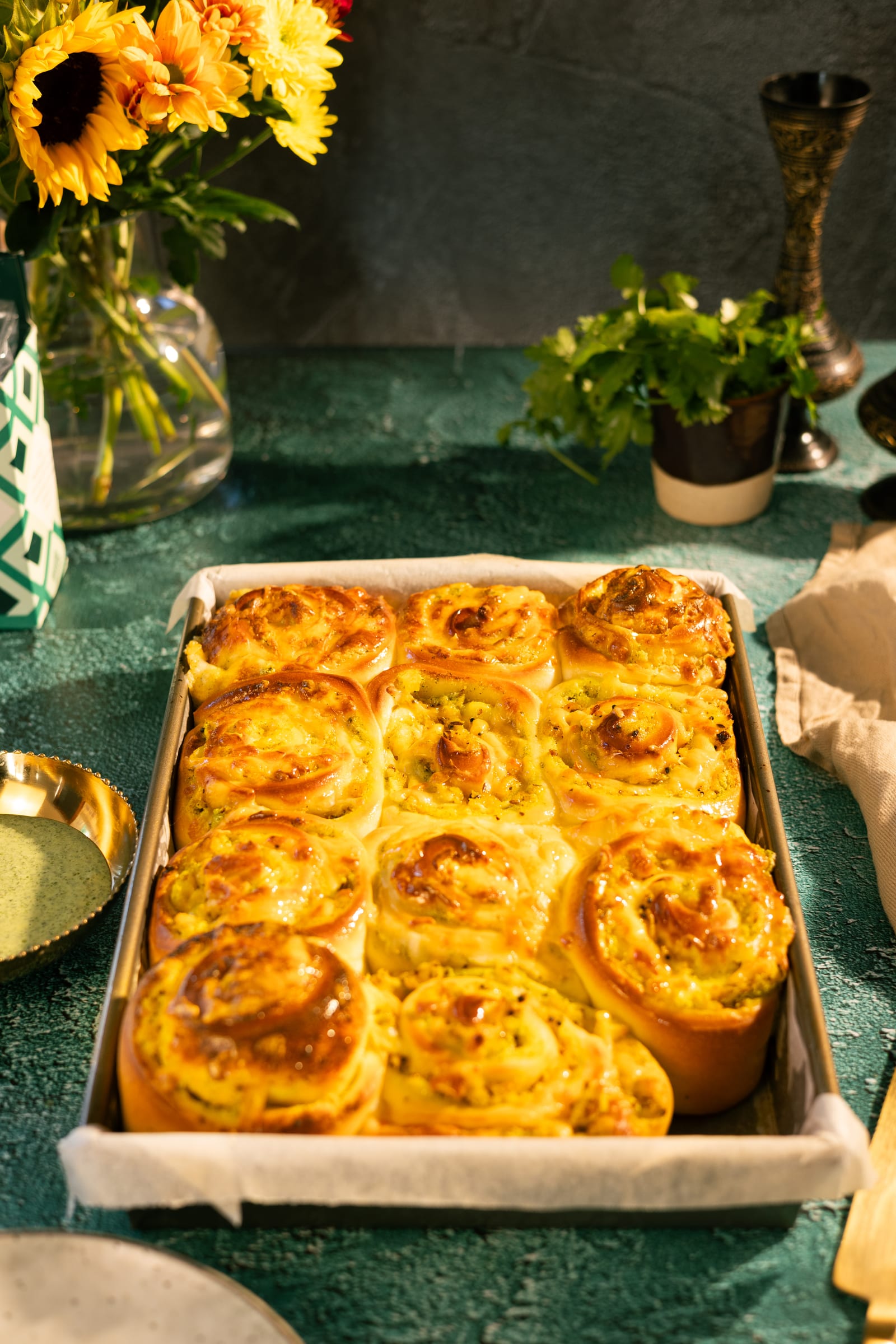 A tray of baked jeera aaloo scrolls with sunflowers behind