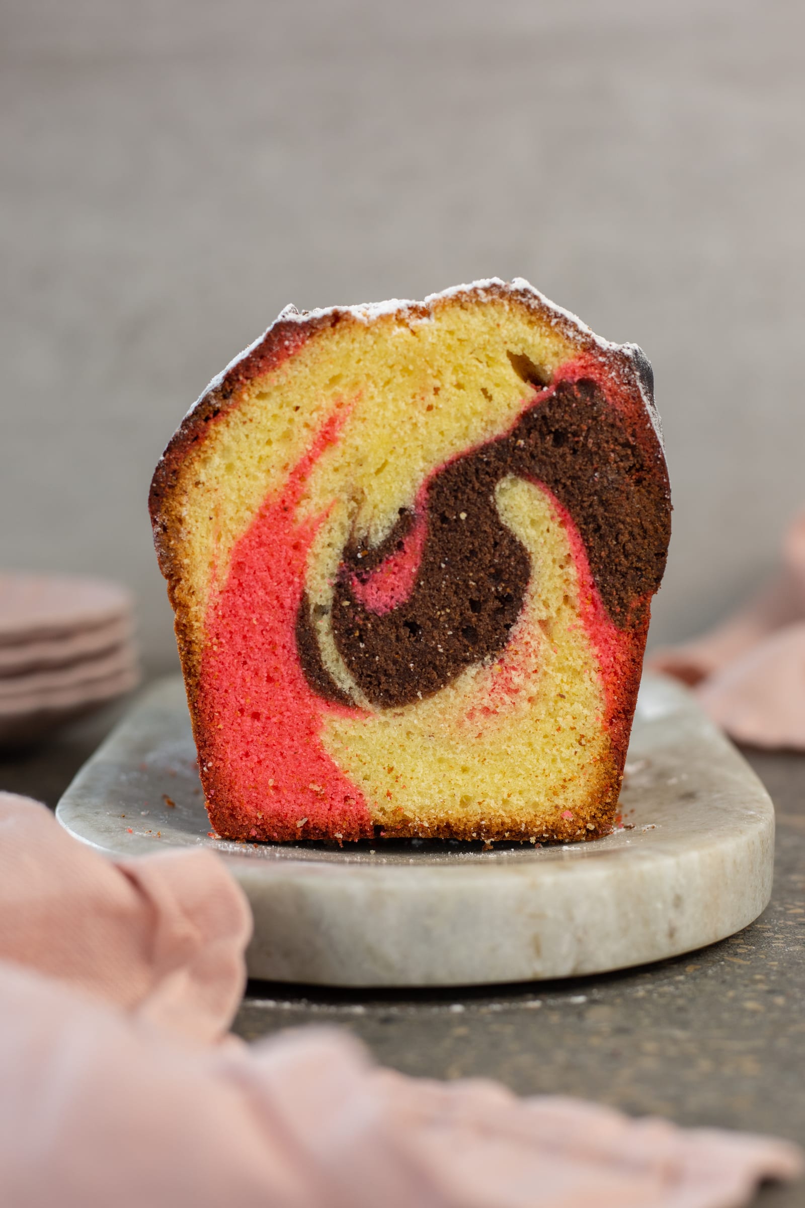 A thick slice of Neapolitan pound cake standing upright, its pink, chocolate and vanilla swirl on show