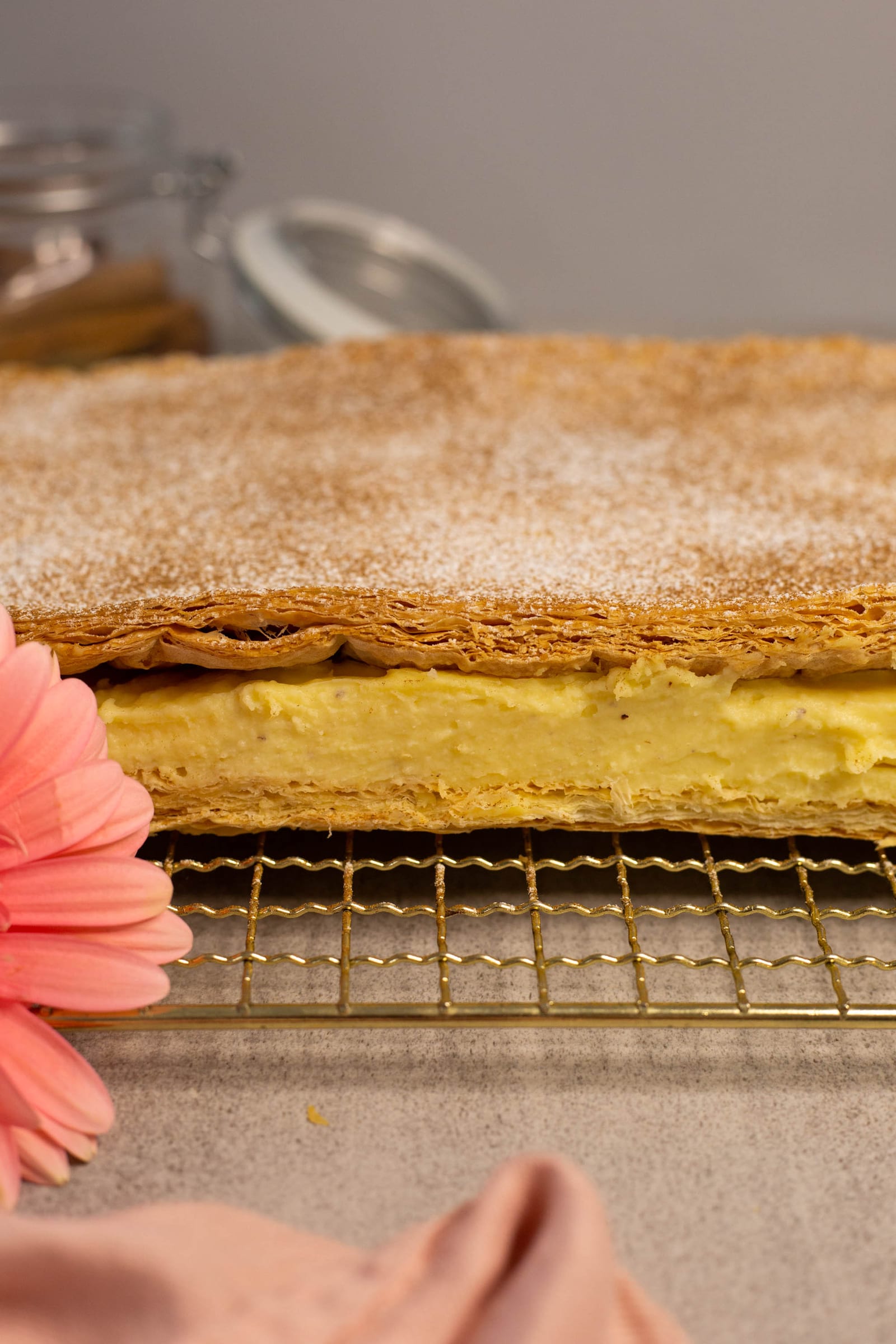 Close-up of the uncut slab of milk tart slices on its rack, a pink gerbera beside it