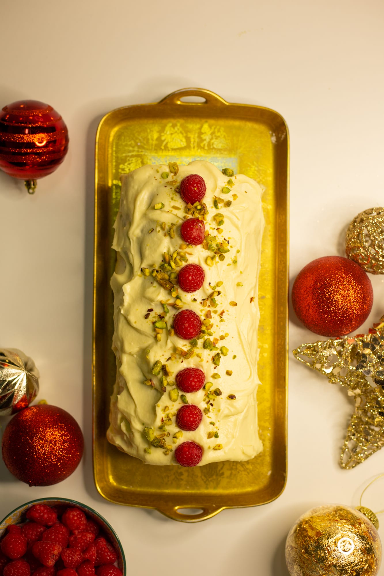 A raspberry and pistachio roulade topped with a line of raspberries on a gold tray, from above