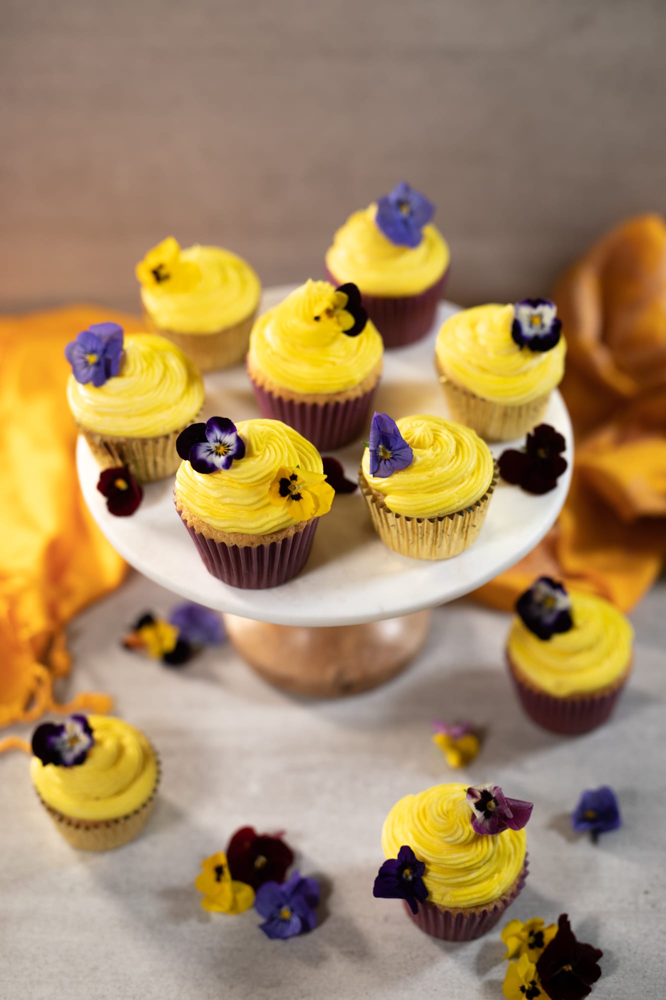 Vanilla cupcakes on a cake stand, with more scattered below