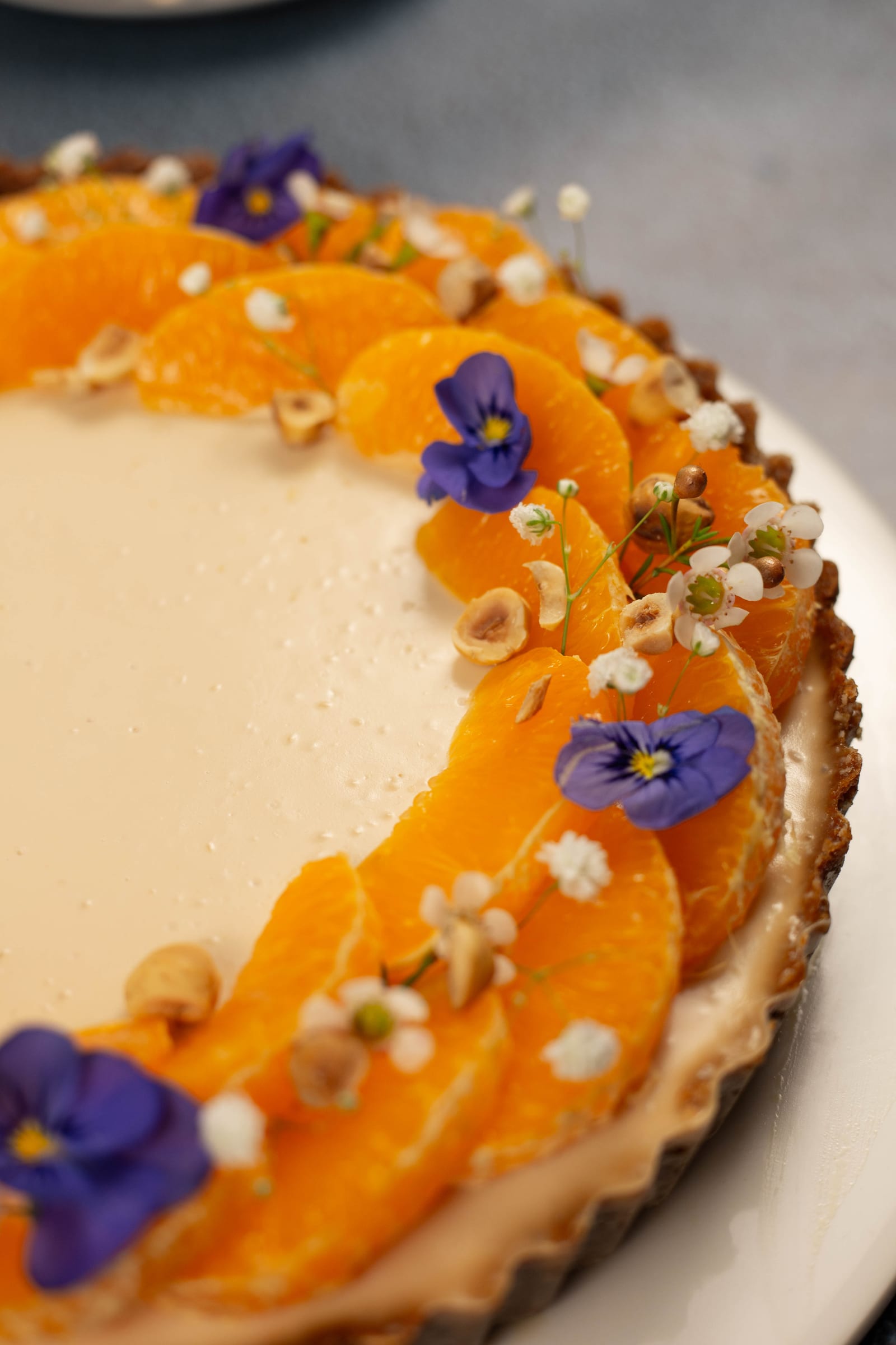 Close-up of clemengold segments, violets and hazelnuts on the tart