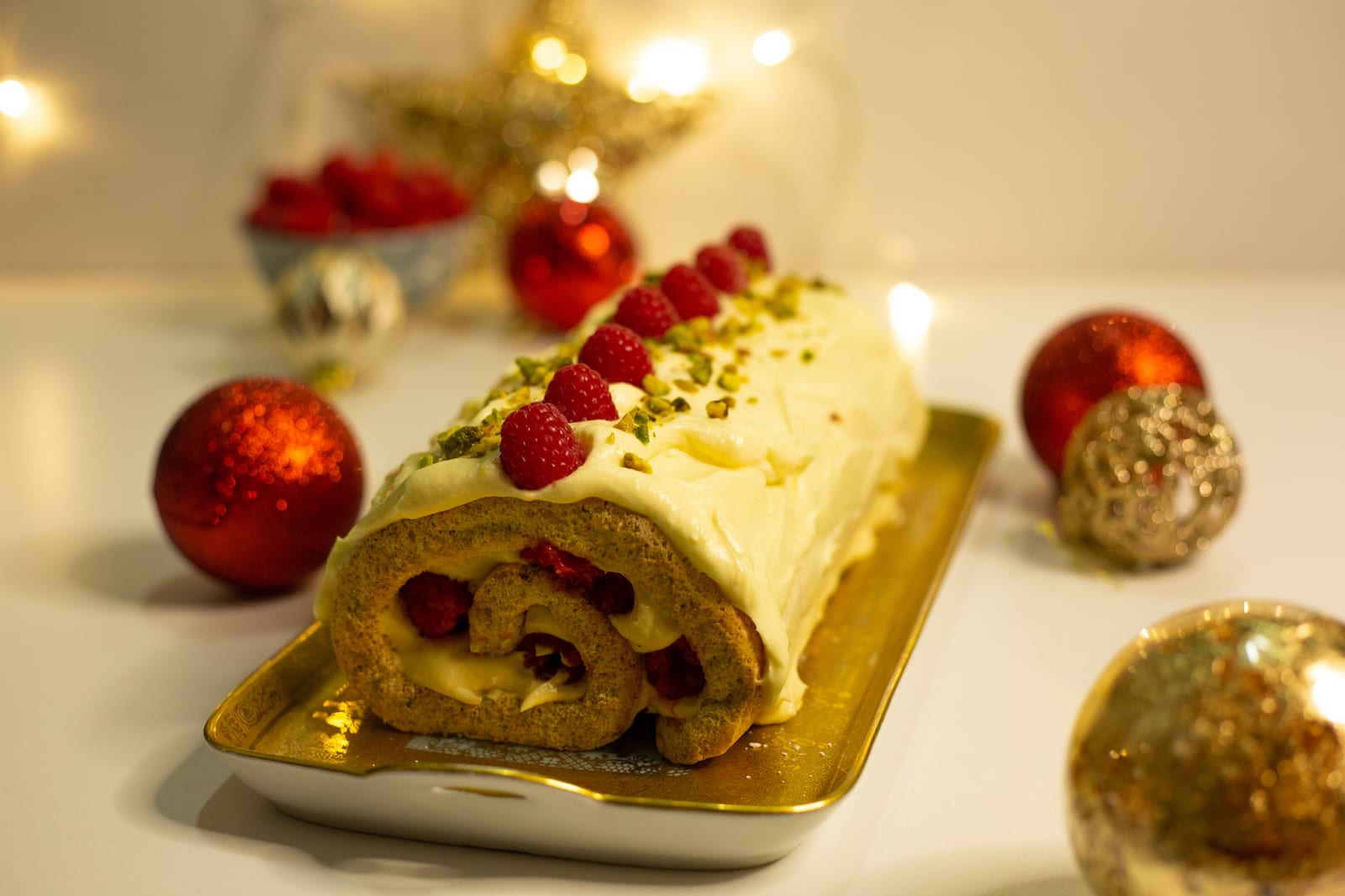 A raspberry and pistachio roulade on a gold tray with red baubles and a gold star