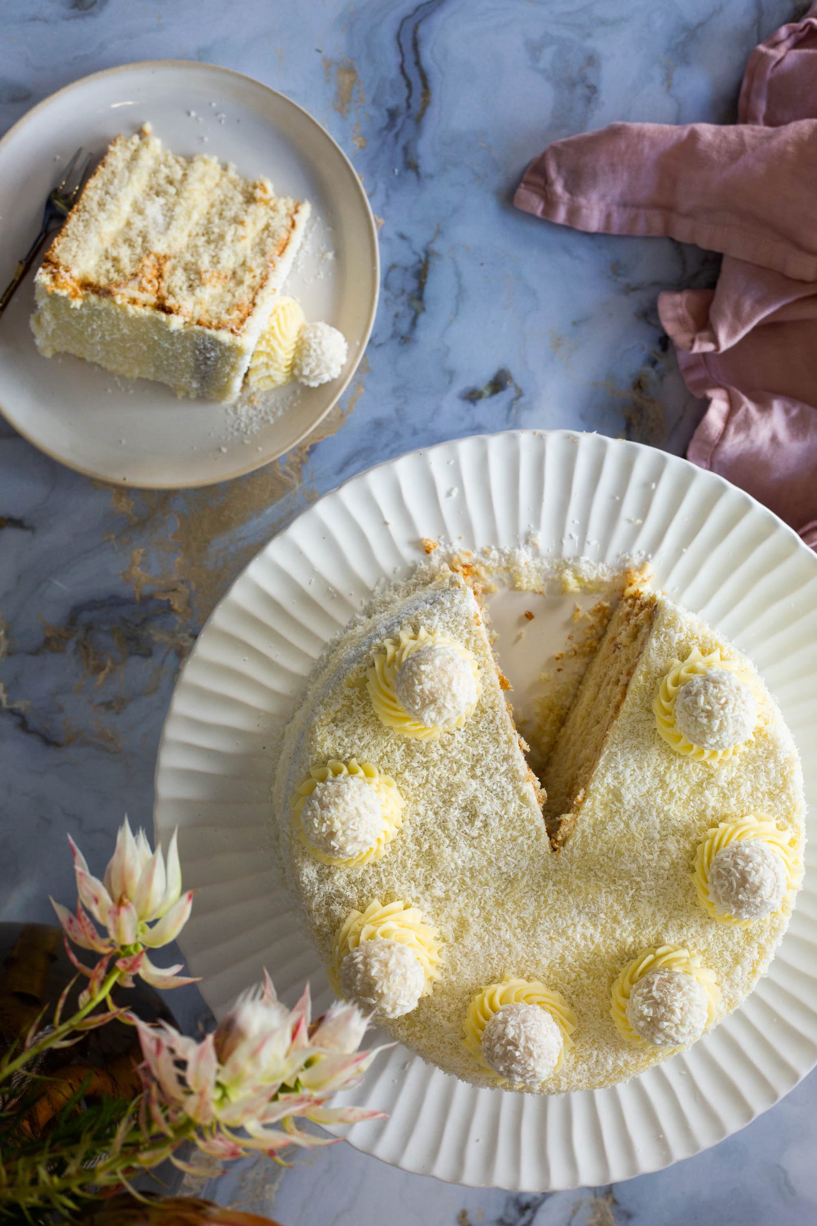 A Raffaello cake with a wedge cut out and a slice on a side plate, proteas around, from above