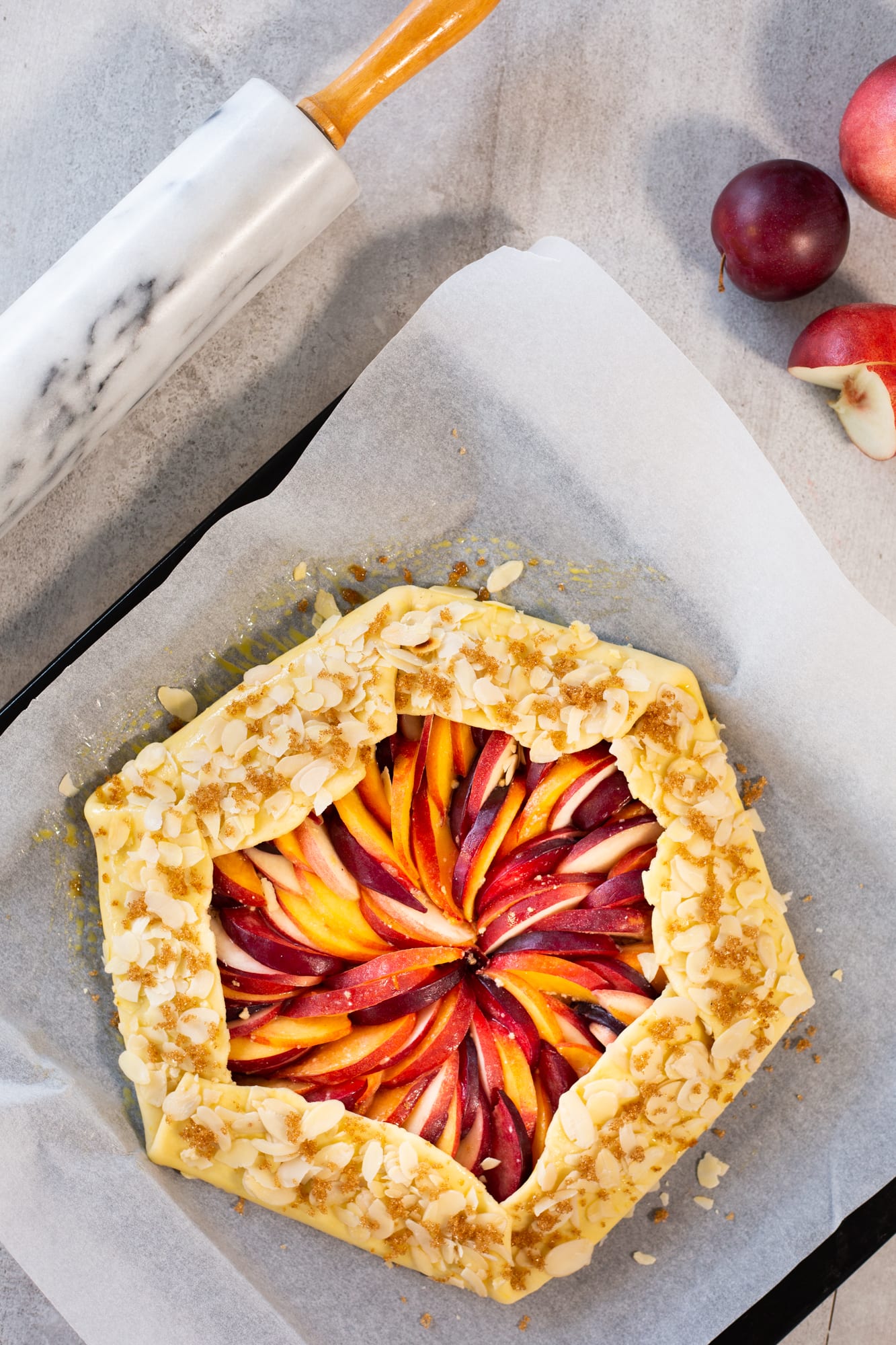 The unbaked stone fruit galette with its pleated edge sprinkled with flaked almonds, from above