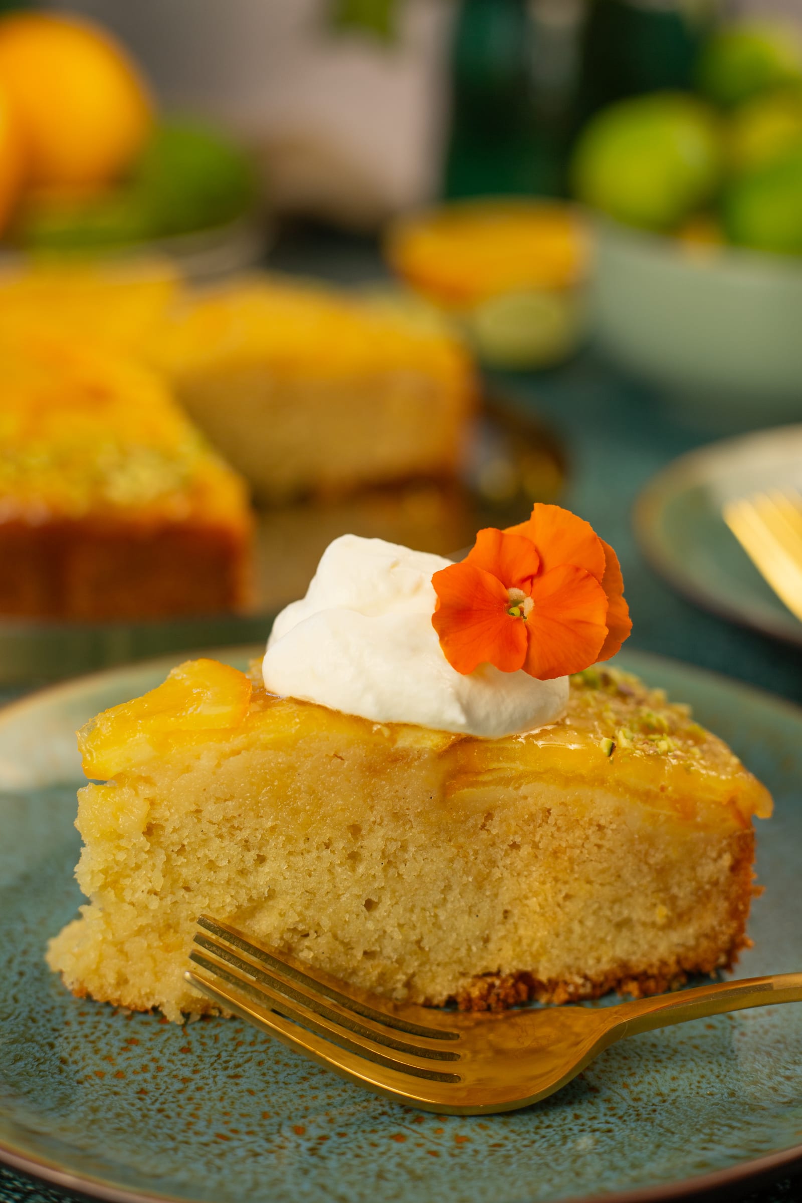 A slice of orange and olive oil upside down cake topped with cream and an orange nasturtium