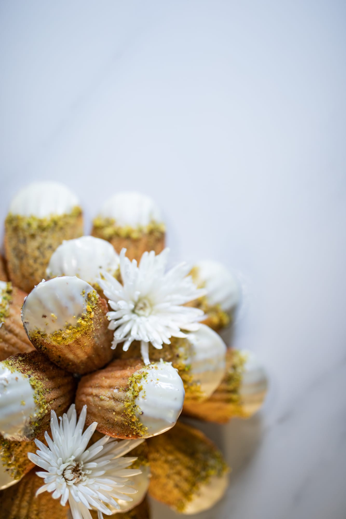 A mound of lemon and poppyseed madeleines with white flowers on marble