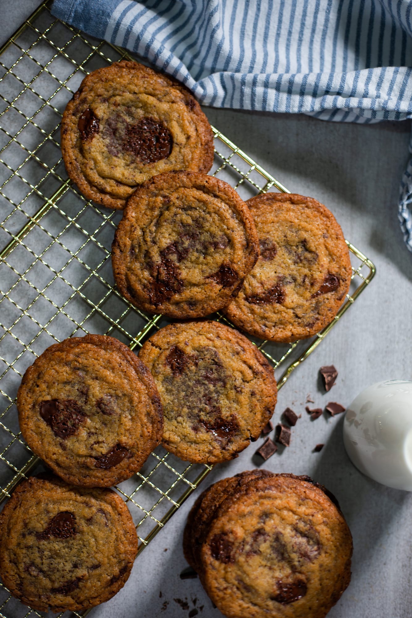 Pan banging chocolate chip cookies on a gold rack with a striped towel, from above