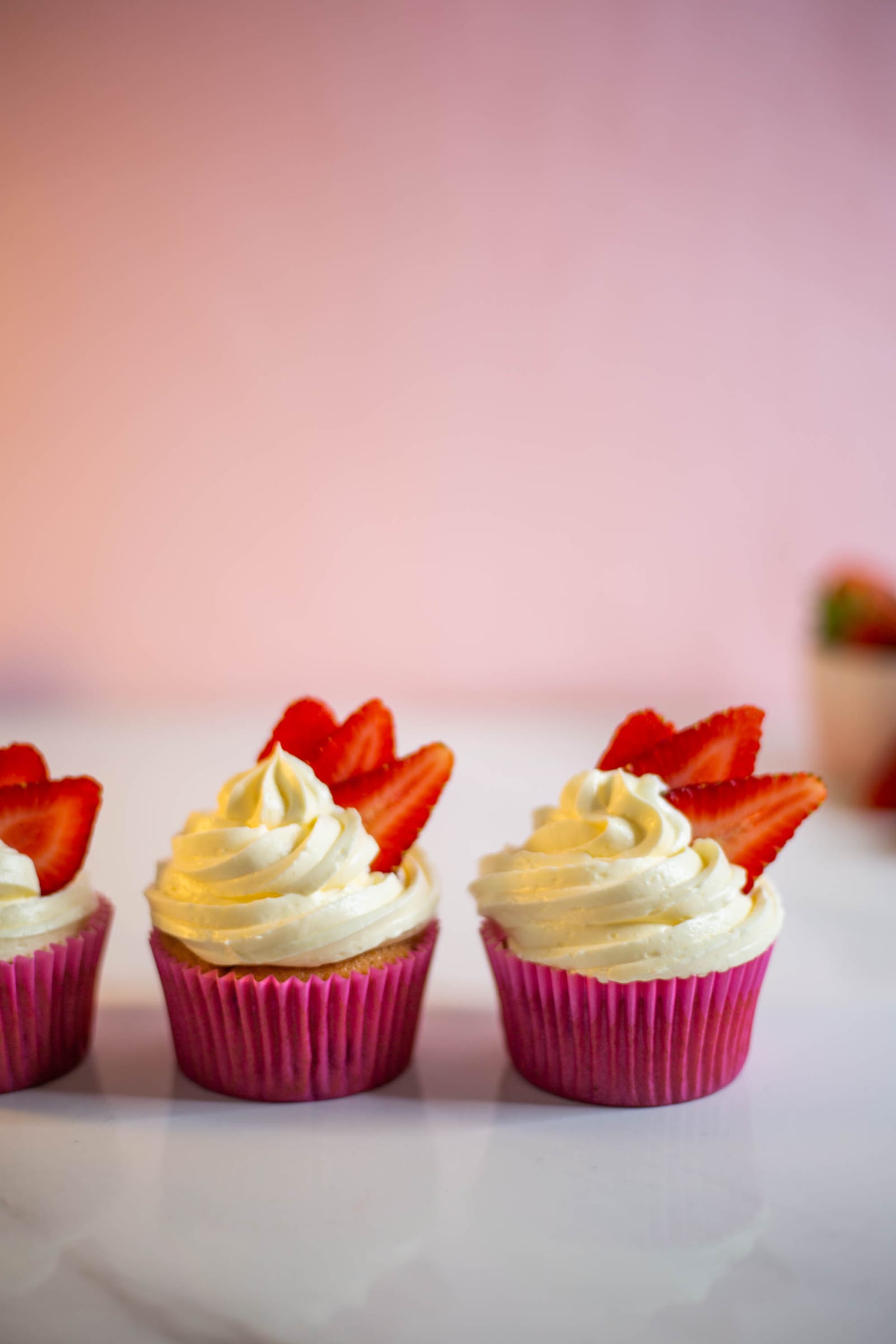 Three strawberry and white chocolate cupcakes in a row on marble