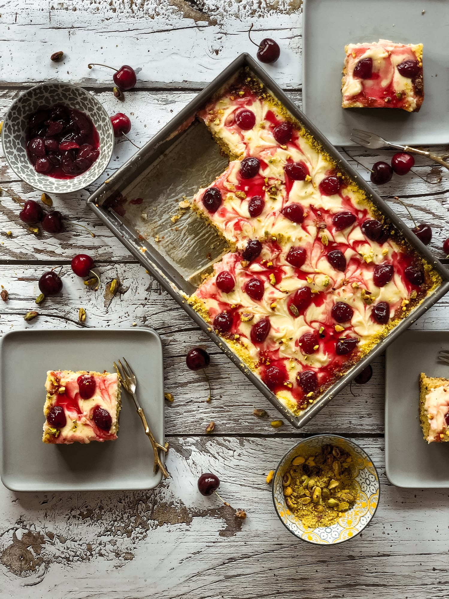 A pistachio and cherry sheet cake with squares taken out, a square on a grey plate, from above