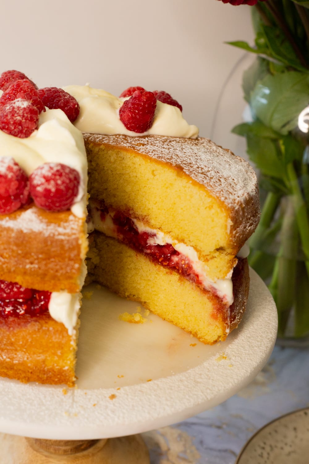 The cut face of a Victoria sandwich, showing the golden sponge, raspberry compote and whipped cream