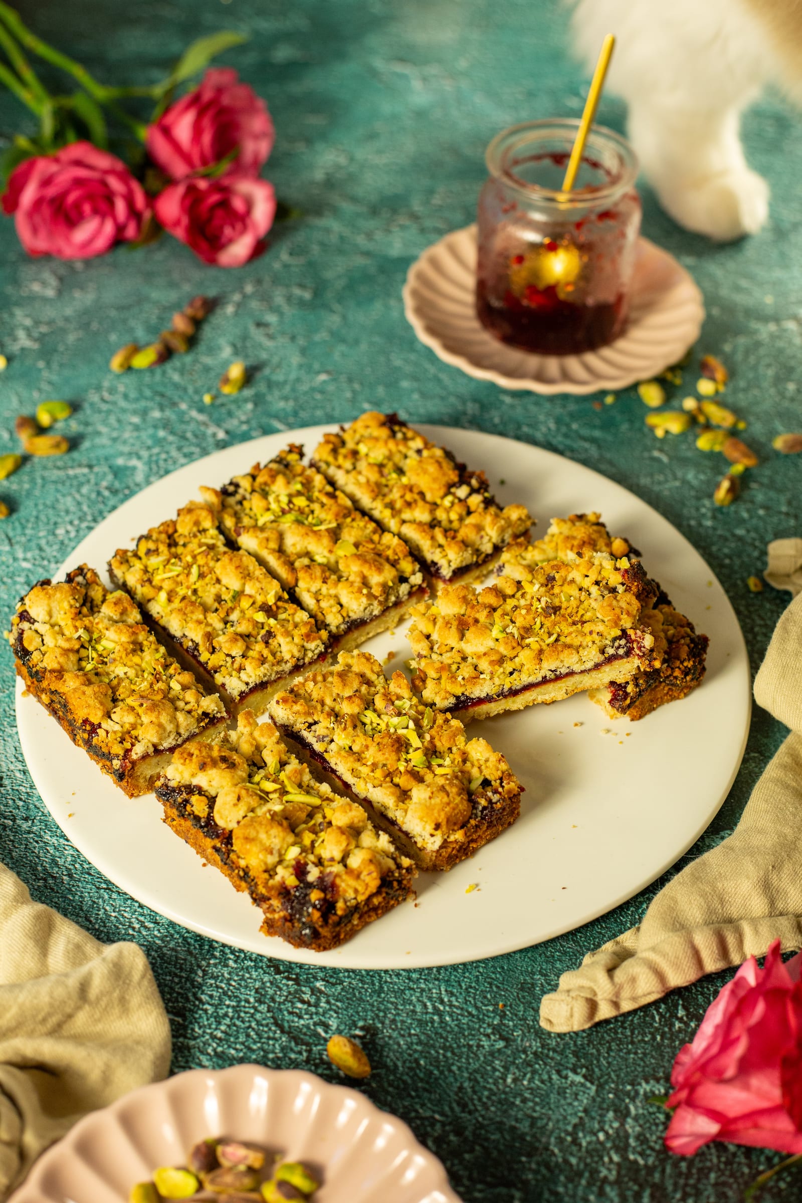 A plate of plum and pistachio Hungarian tart bars with a candle and pink roses