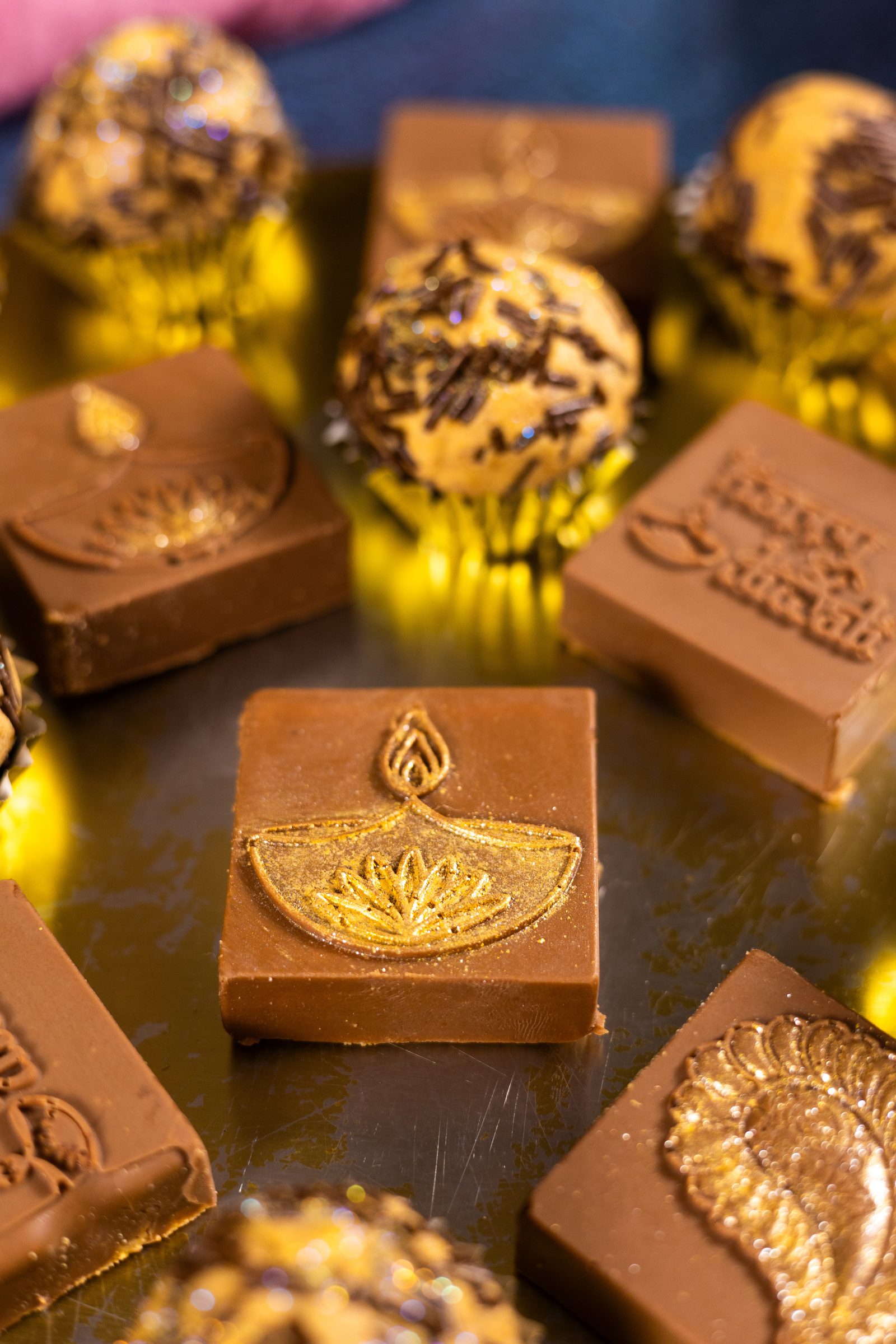 Close-up of a caramel and chocolate Simply Wonderful with a gold diya on top, beside round ones in gold cases