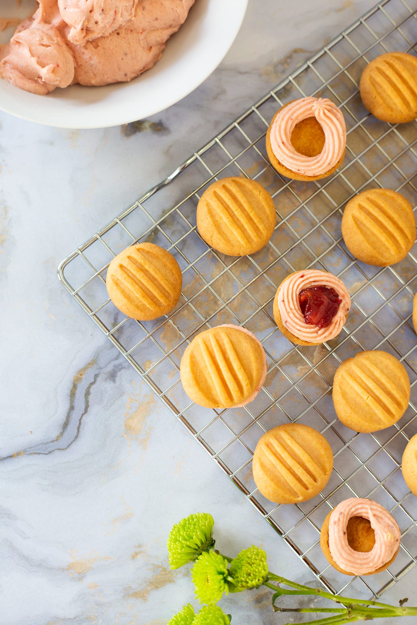 Plain and ringed custard biscuits on a wire rack beside a bowl of filling, from above