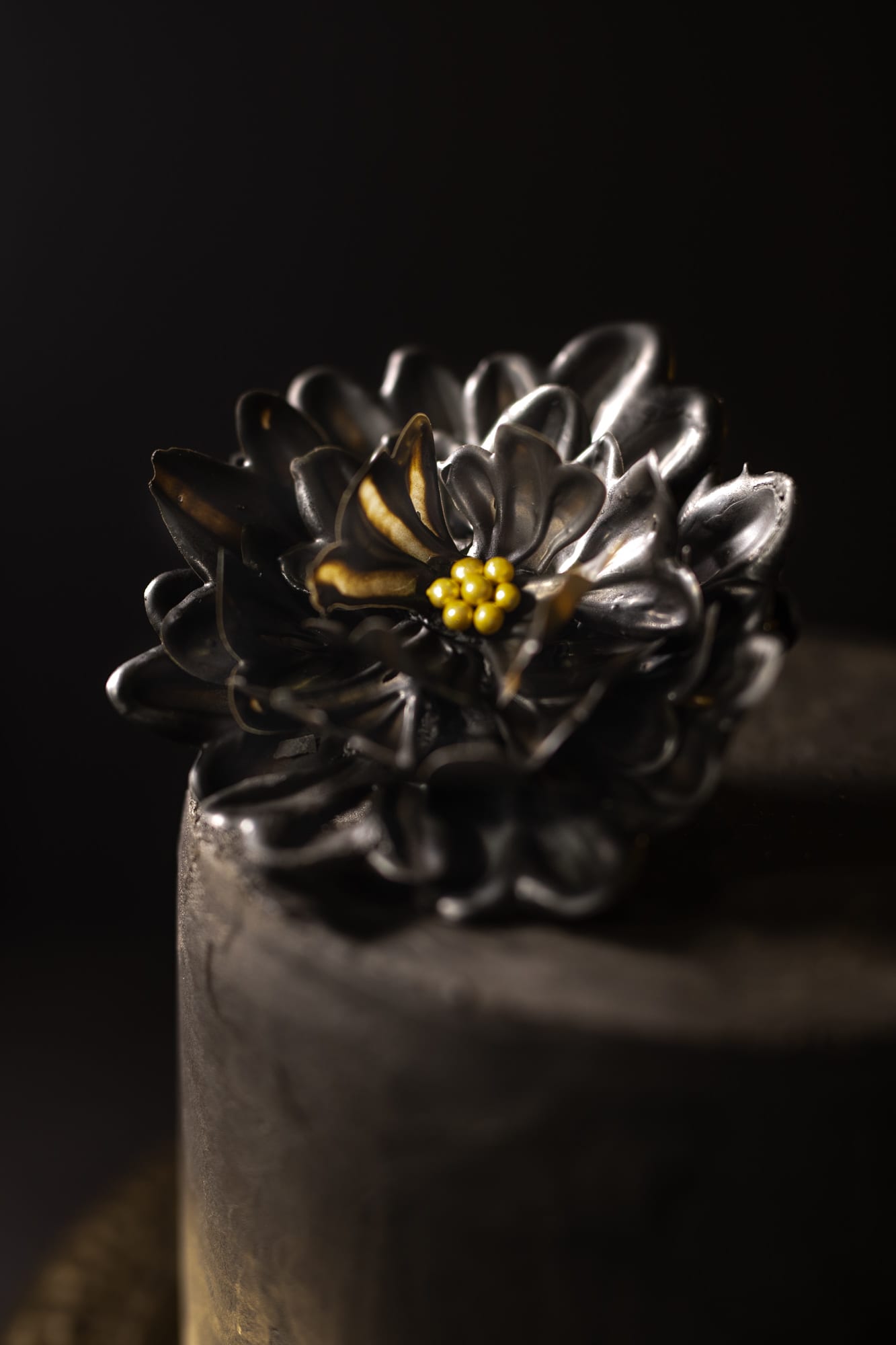 Close-up of the dark chocolate flower with its gold centre on a black cake