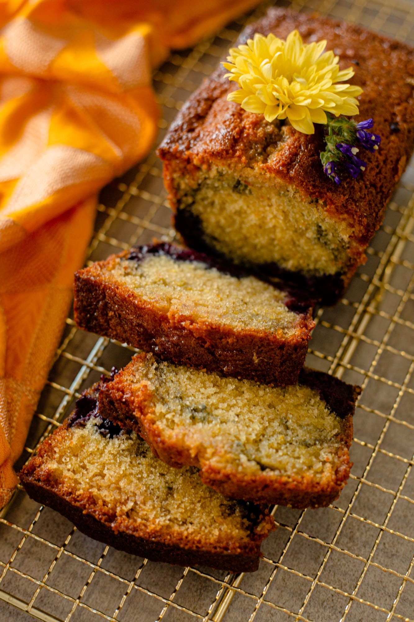Slices of lemon and blueberry loaf fanned out, a yellow flower beside them, from above