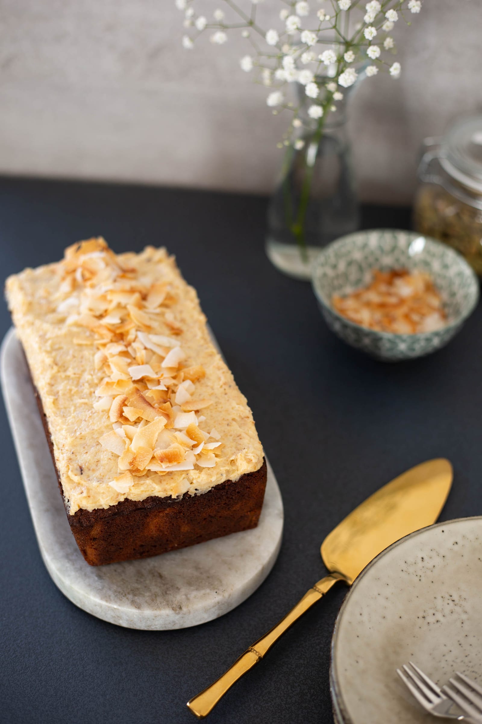 A frosted gluten-free coconut loaf on its marble board, from slightly above