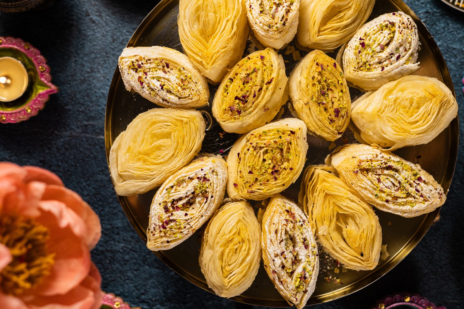 Banana puri on a gold tray with a peony and diyas, from above