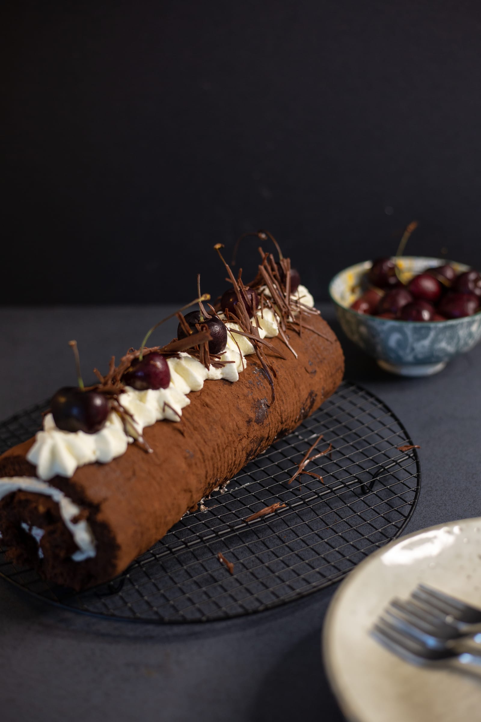 A Black Forest Swiss roll decorated with cream rosettes, cherries and chocolate on a black rack