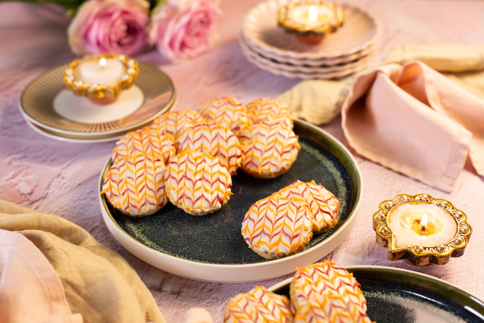 Coconut and almond biscuits with chevron icing on a dark plate, with roses and diyas