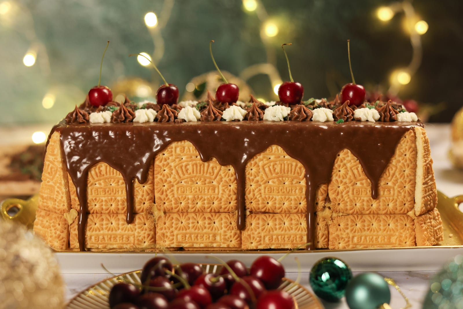A peppermint crisp loaf dripping with chocolate ganache and topped with cherries, under fairy lights