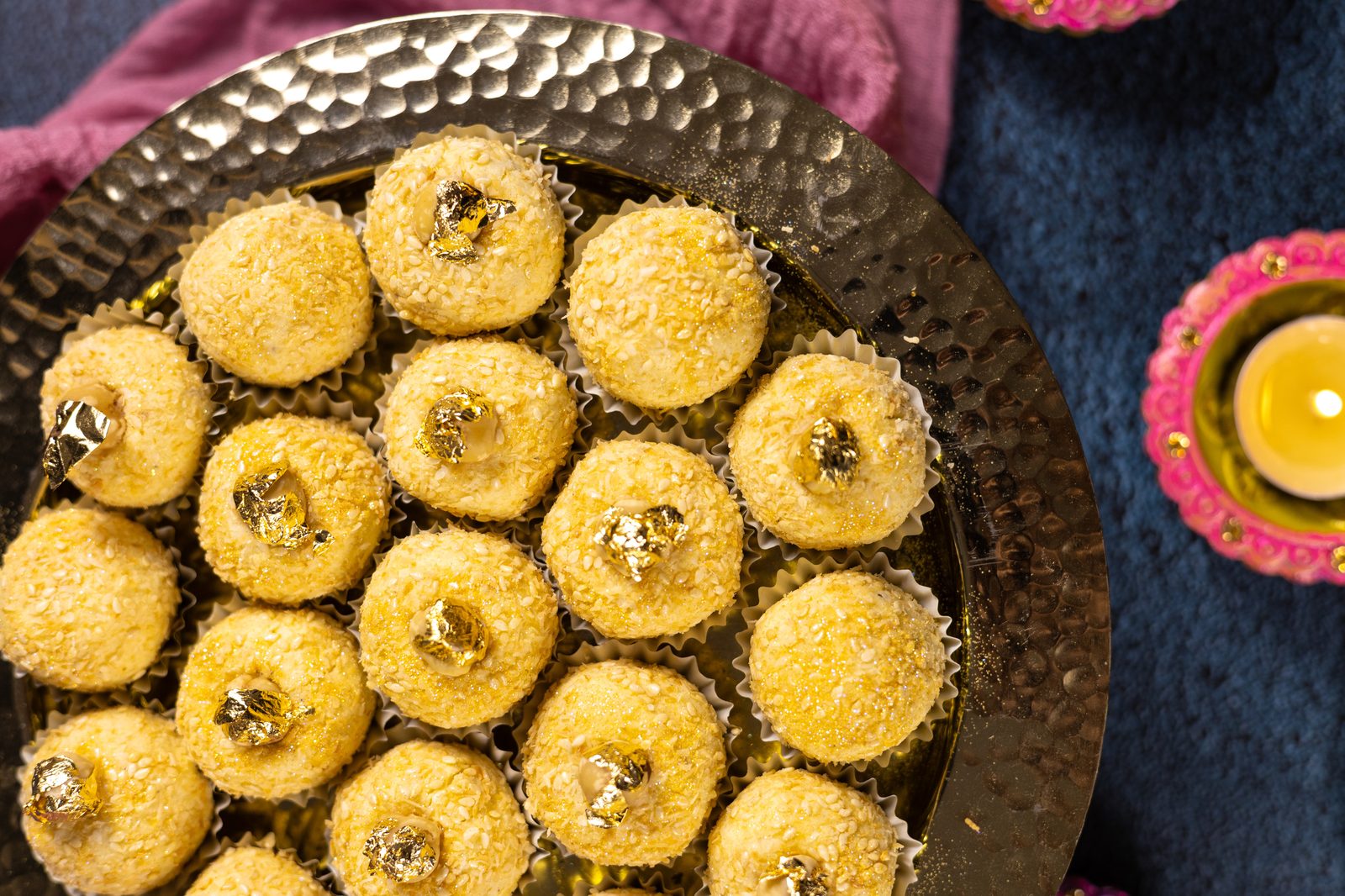 Coconut Simply Wonderfuls in paper cases on a hammered copper platter beside a lit diya, from above