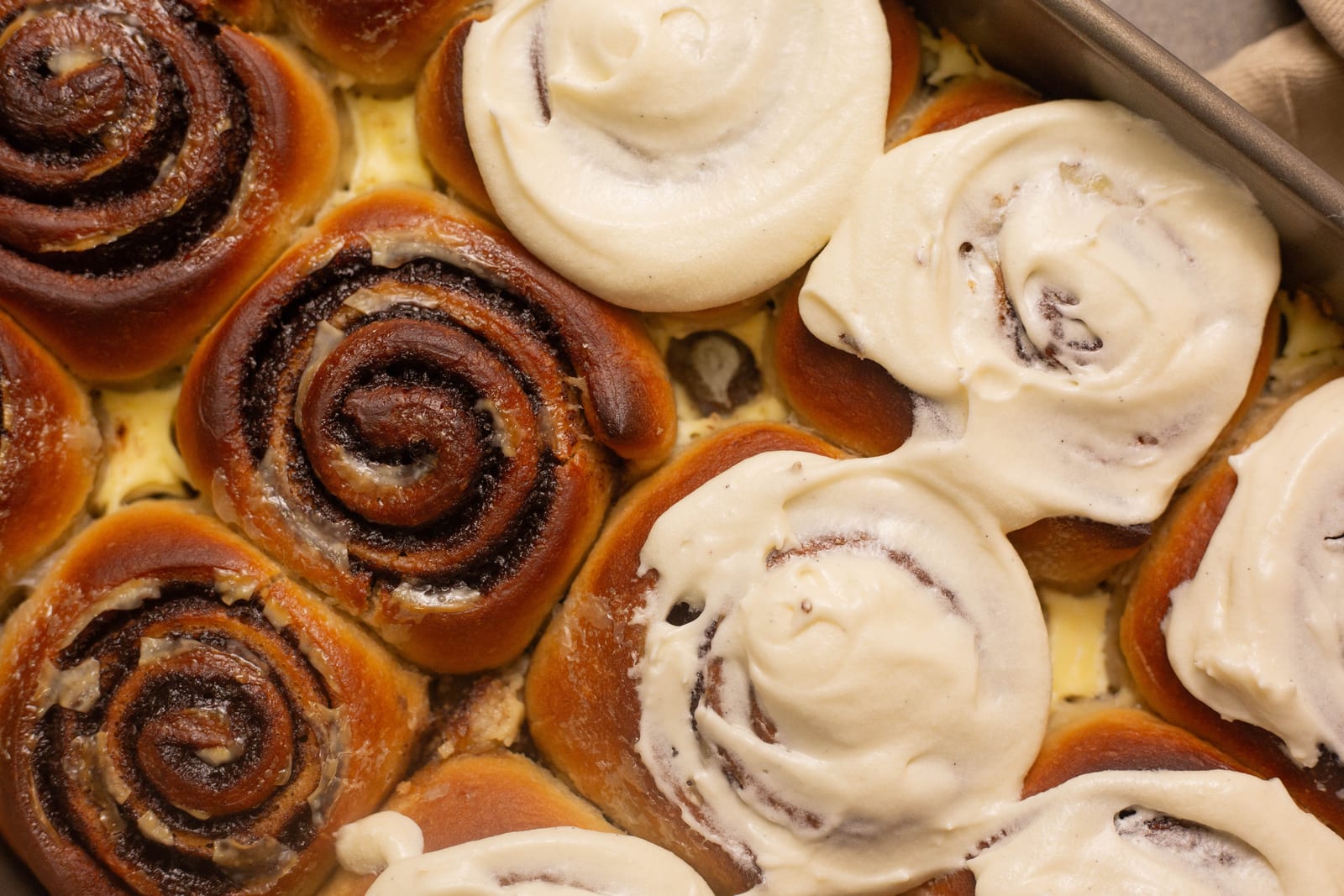 Cinnamon rolls in a tin, some swirled with cream cheese icing