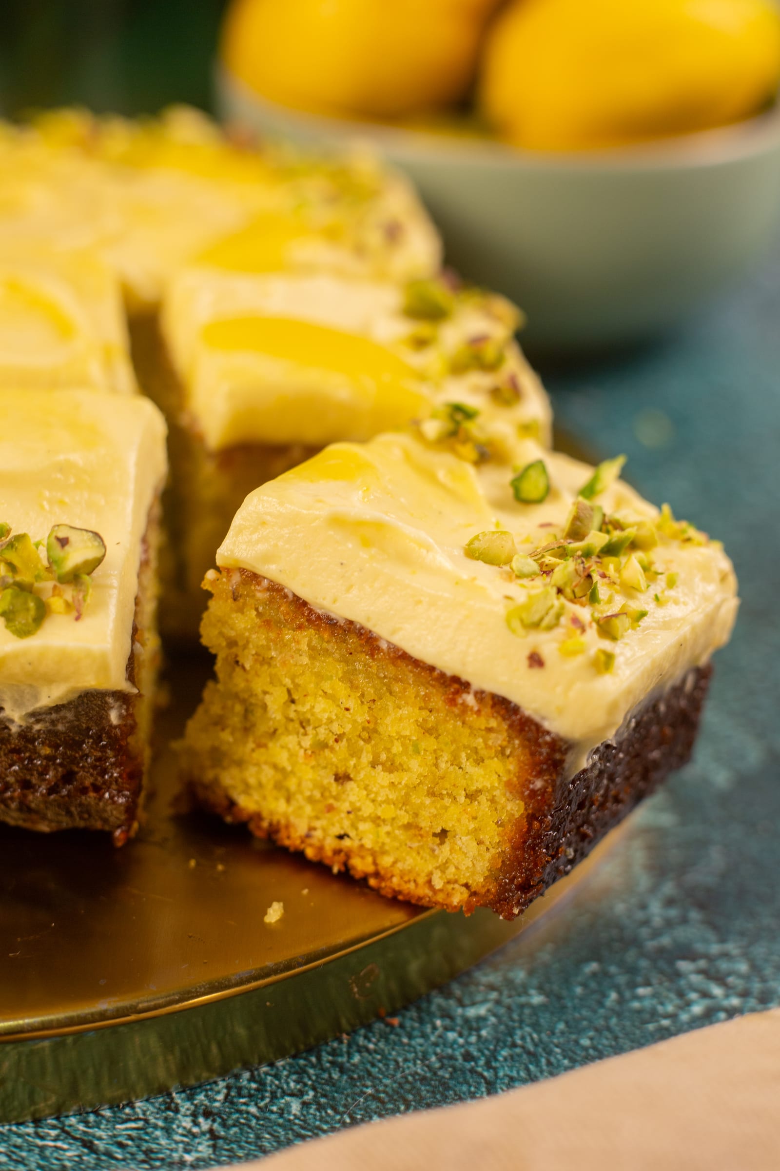 Close-up of cut squares of pistachio and lemon traybake, showing the moist green-flecked crumb
