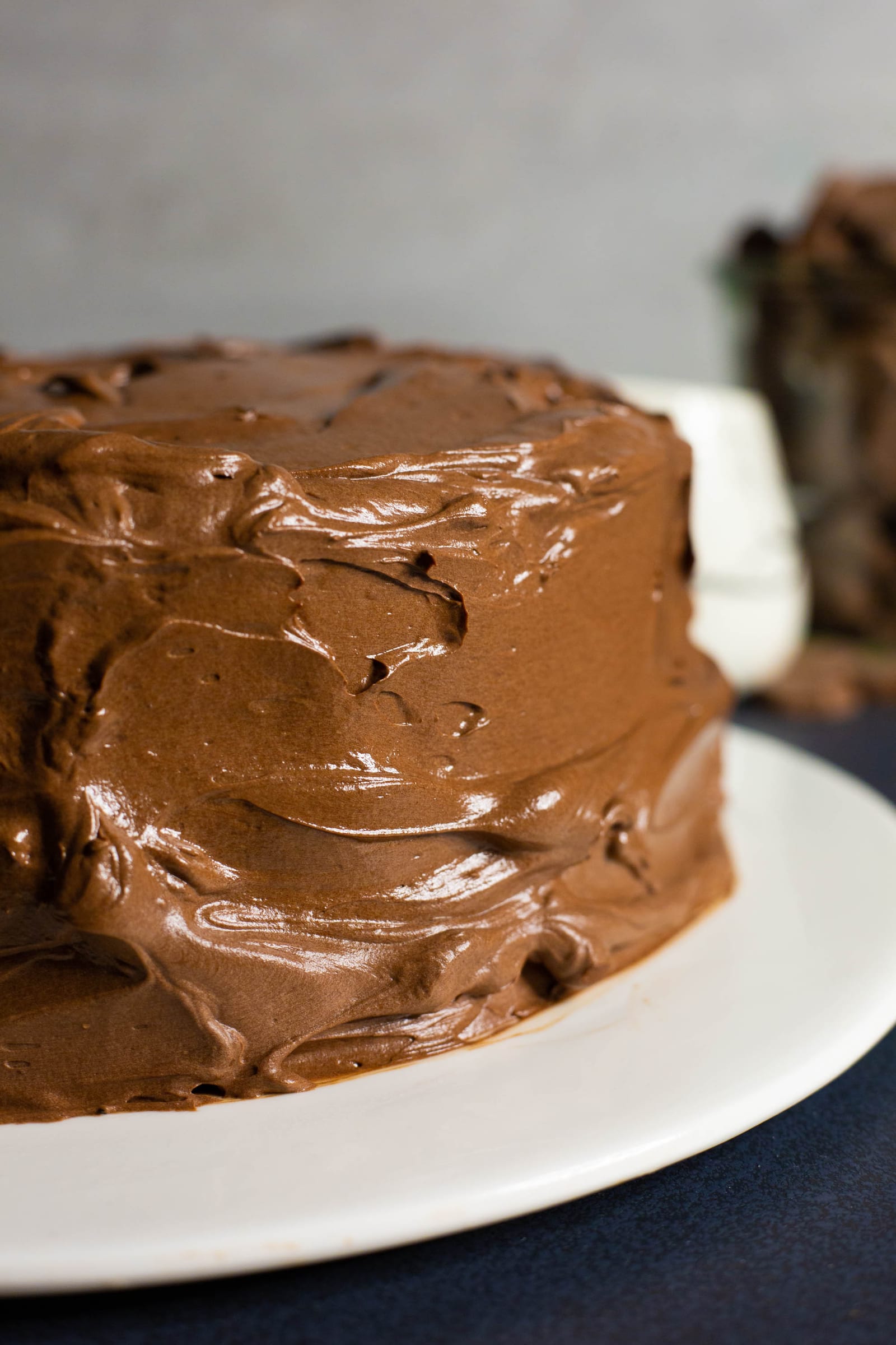 A whole chocolate fudge cake with swirled frosting on a white plate, chocolate buttons around it