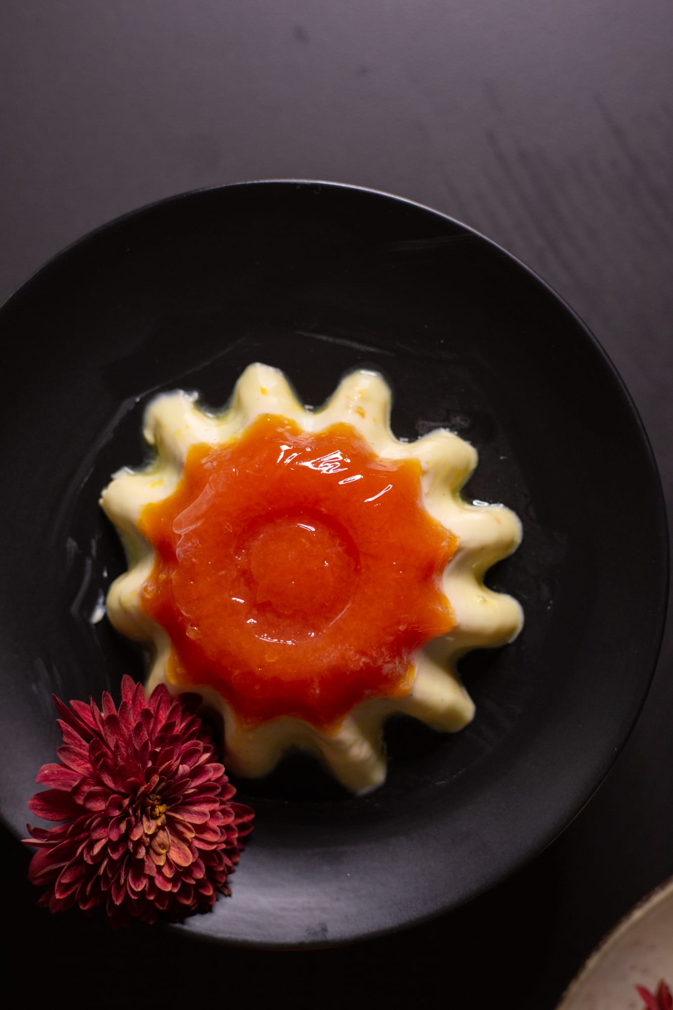 A fluted vanilla yoghurt panna cotta with blood orange jelly on a black plate, from above