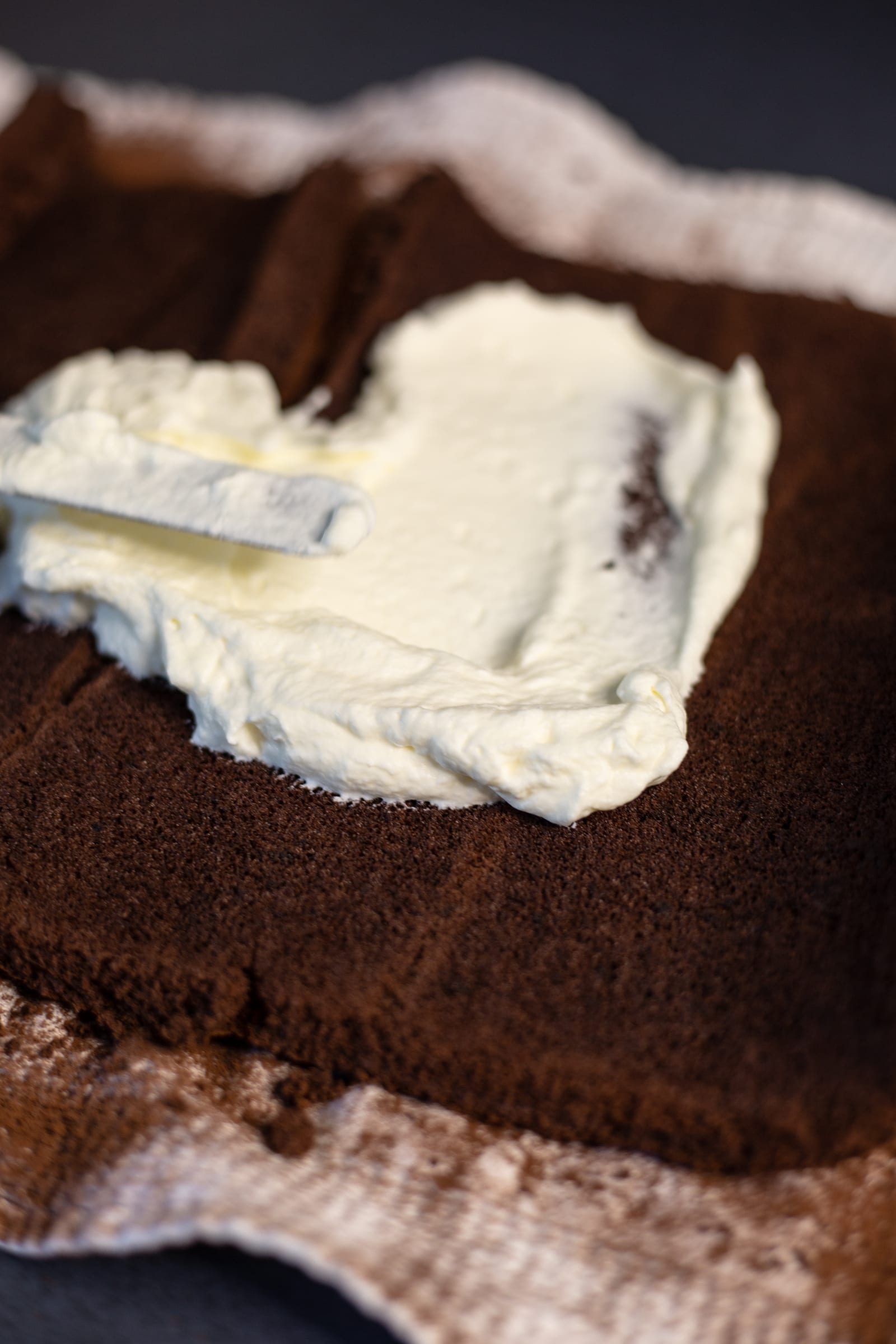 Whipped cream being spread over the chocolate sponge for a Black Forest Swiss roll, from above