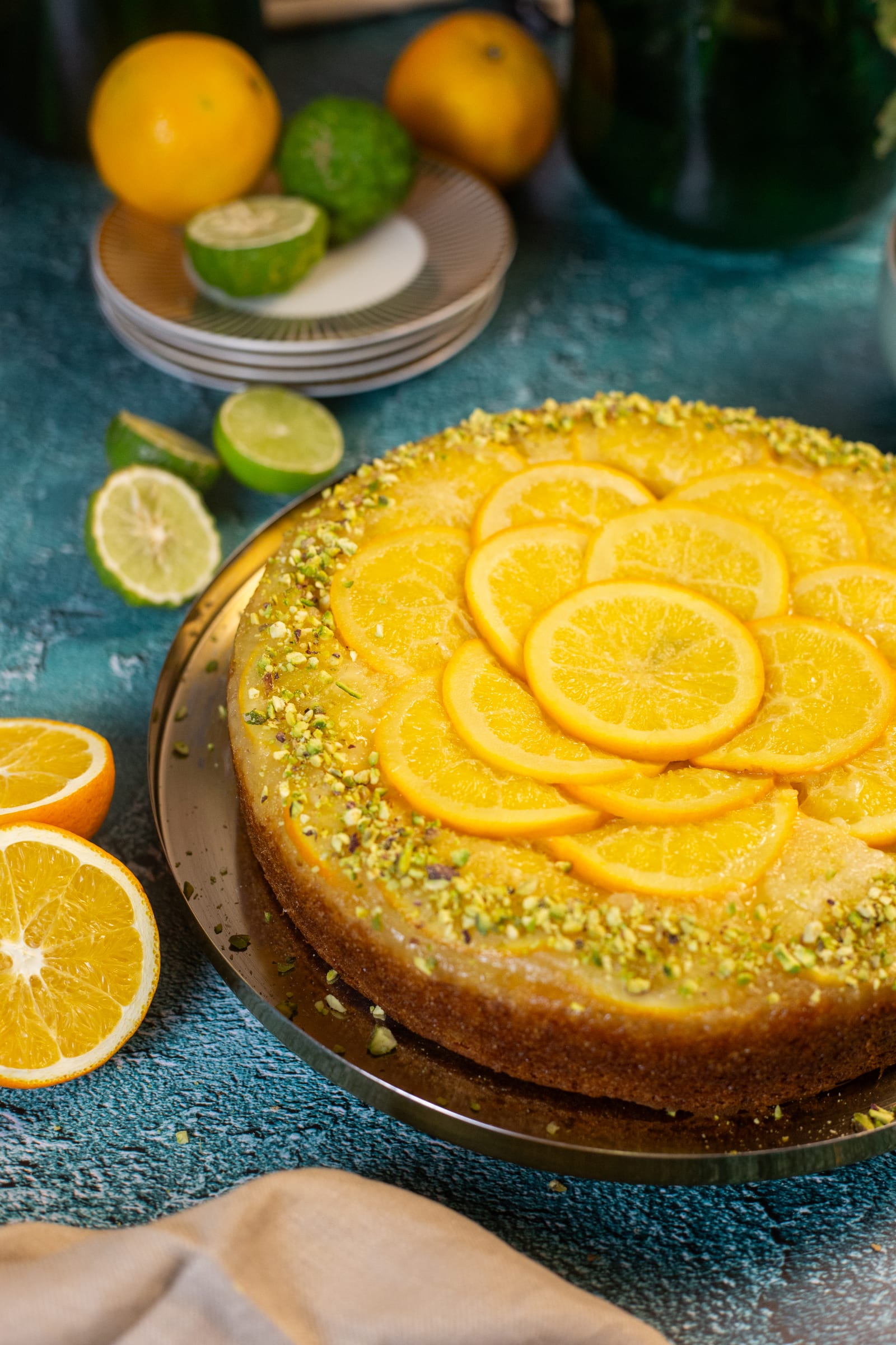 A whole orange and olive oil upside down cake on a gold plate, ringed with chopped pistachios