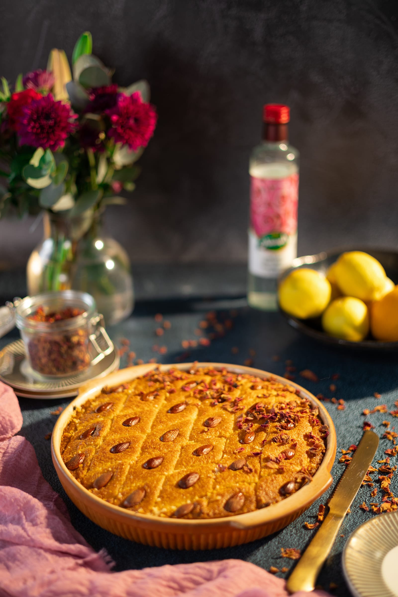 The basbousa with red roses, rose water and lemons behind