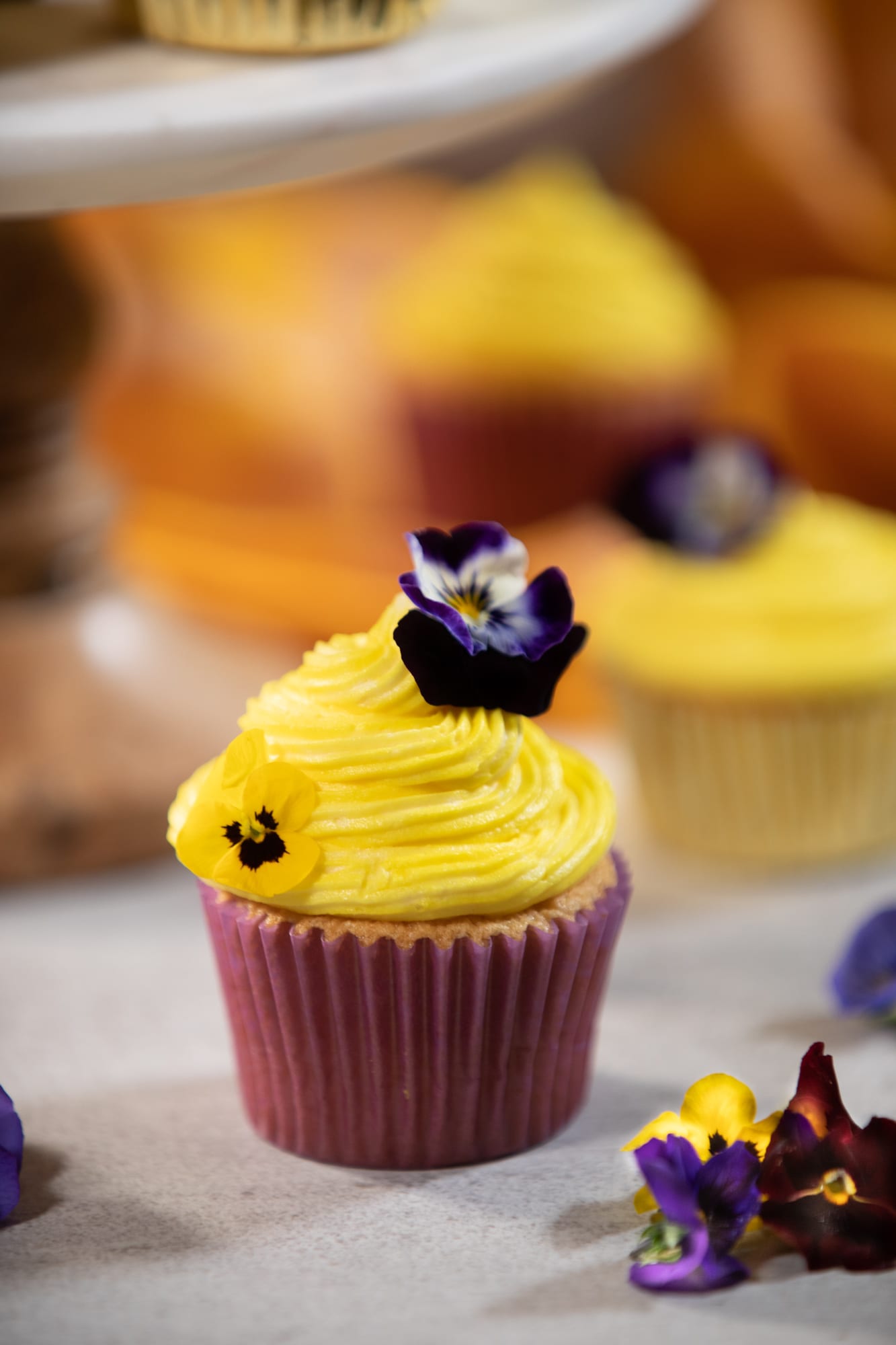 A single vanilla cupcake piped with yellow buttercream and topped with a pansy