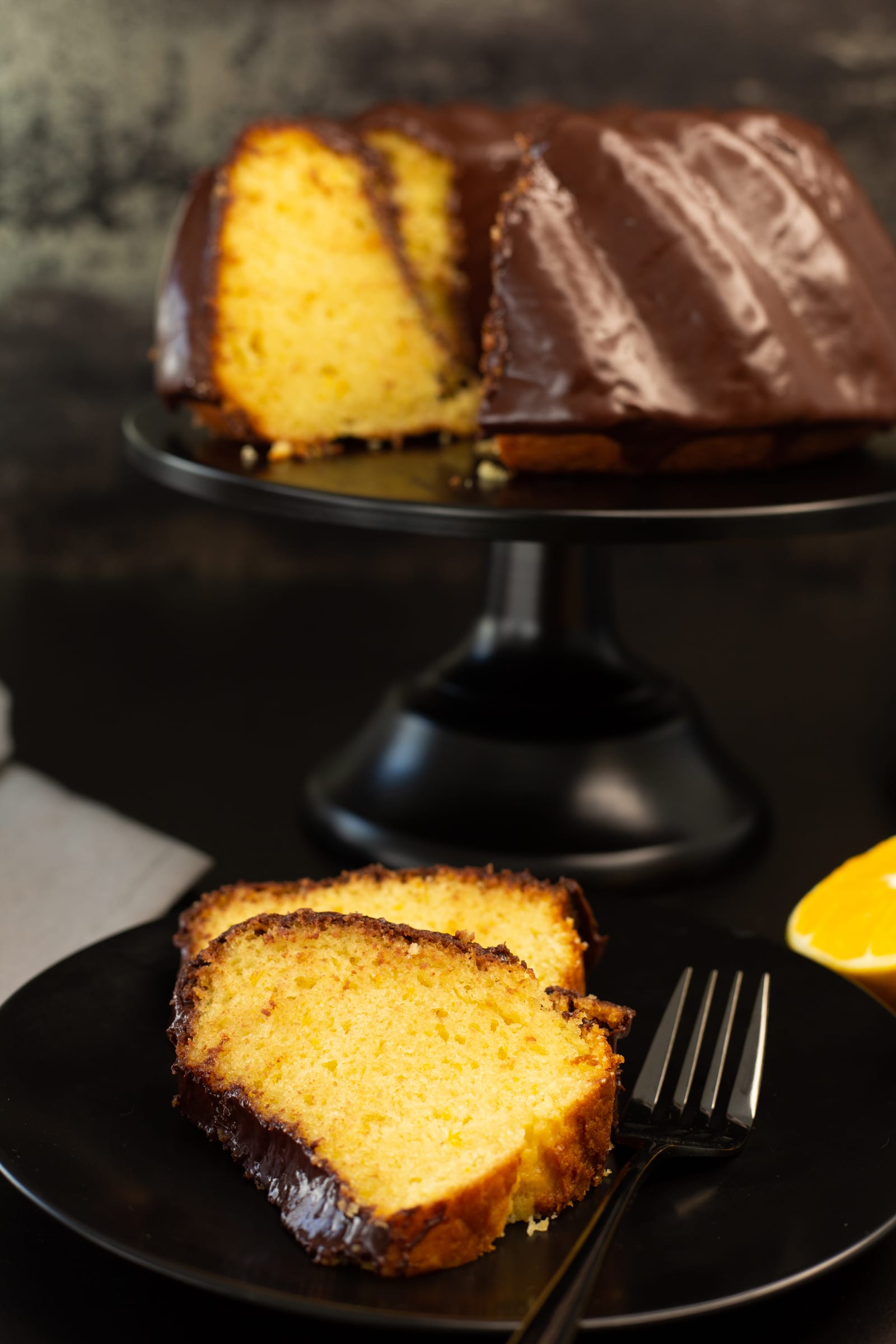 Slices of orange and olive oil bundt showing the soft golden crumb, with the cut cake behind