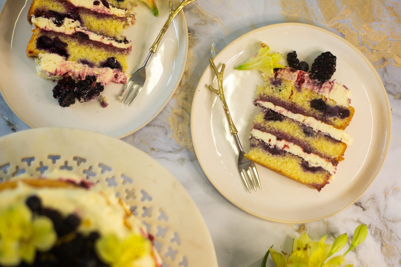 Slices of lemon and blueberry cake on plates with gold forks, from above