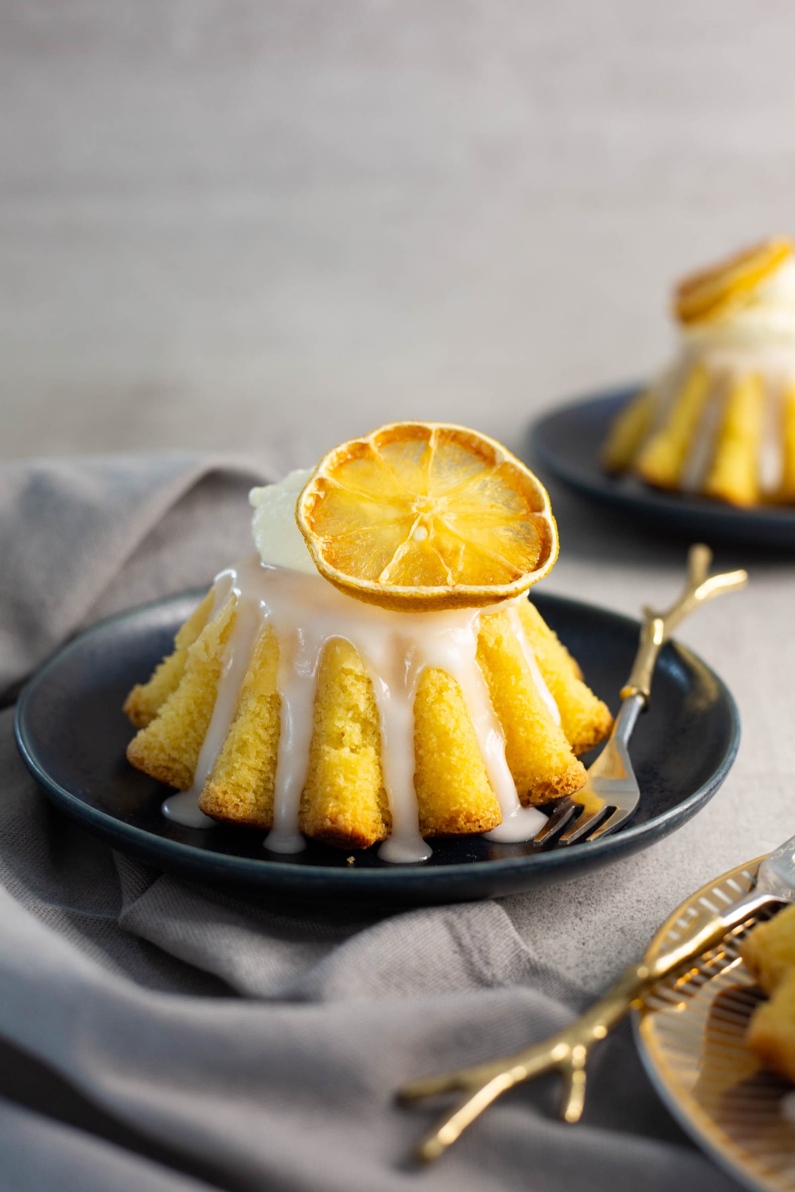 A semolina mini cake with lemon glaze and a dried lemon slice on a dark plate