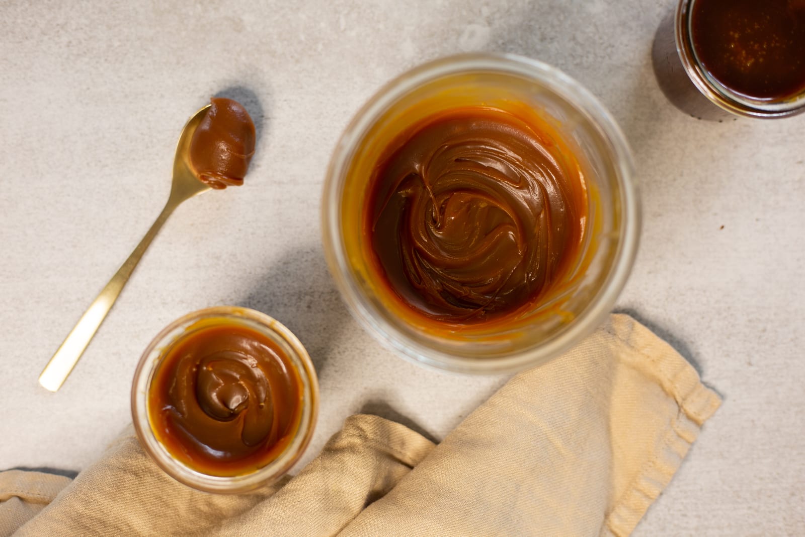 Salted caramel sauce in a glass bowl and a small ramekin, with a gold spoon on a linen napkin