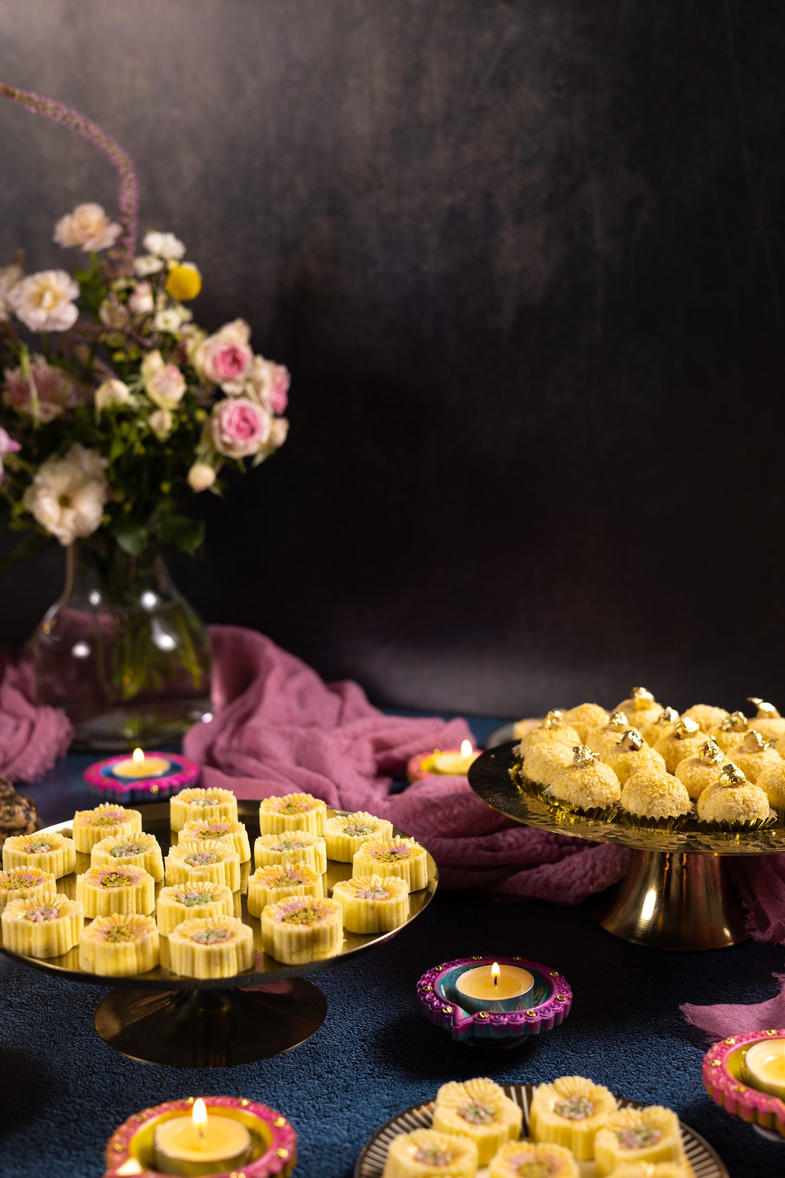 Simply wonderfuls on a gold stand, with diyas and a vase of flowers behind