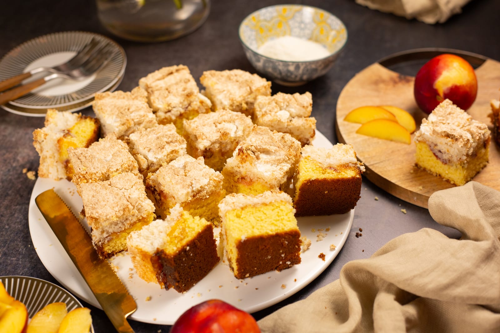 Hertzoggie squares on a white plate, with fresh peaches and a bowl of coconut