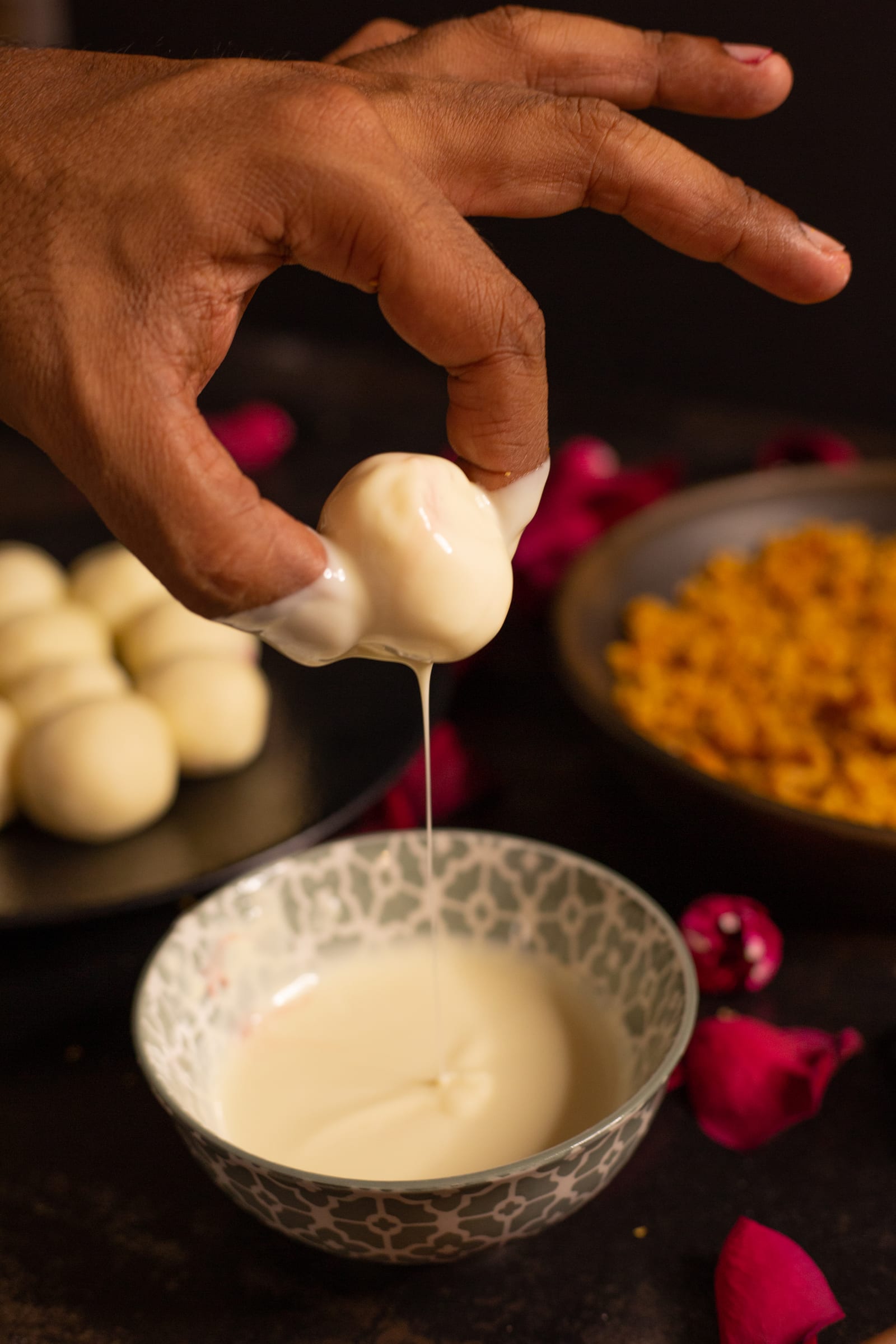 A truffle lifted out of melted white chocolate, dripping back into the bowl