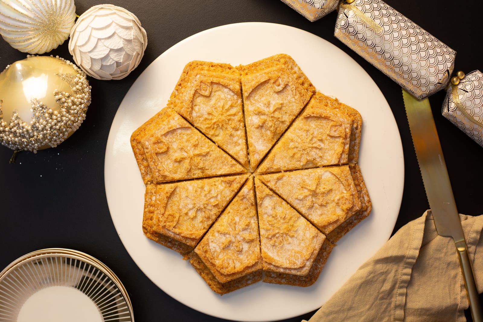 Star-shaped shortbread cut into wedges on a white plate, with Christmas baubles