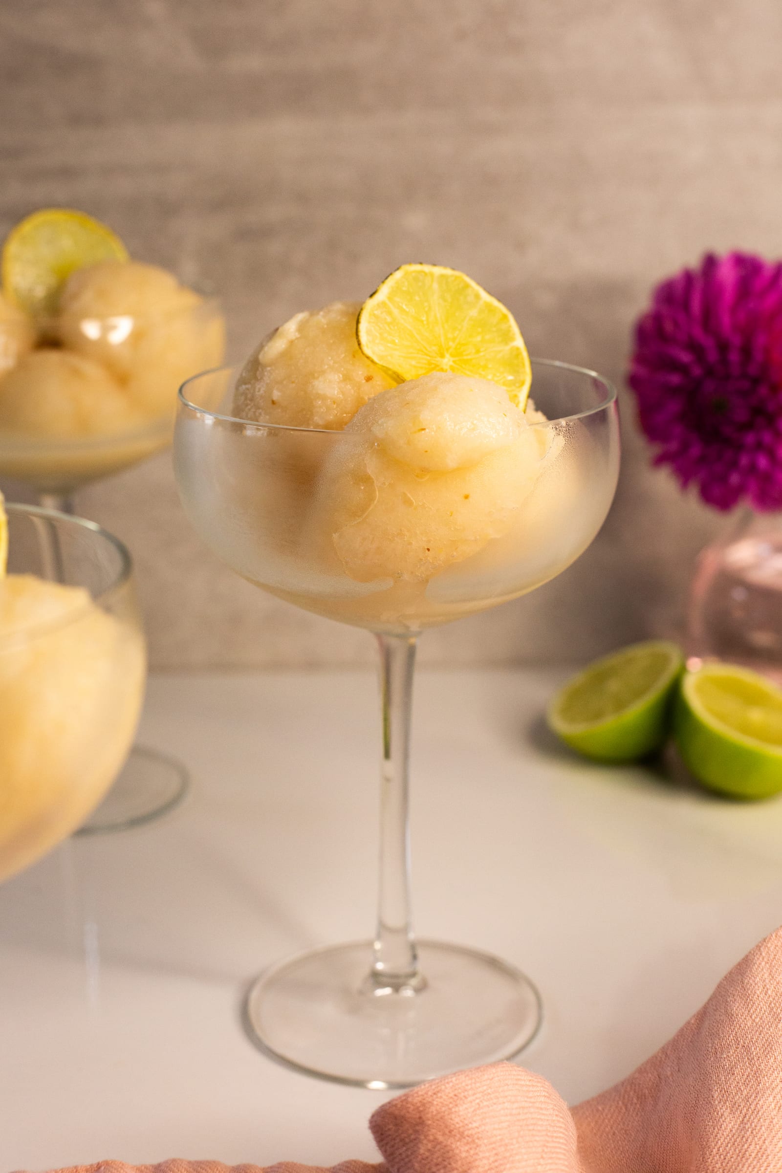 Coupes of litchi and lemon sorbet with citrus wheels, a pink flower behind