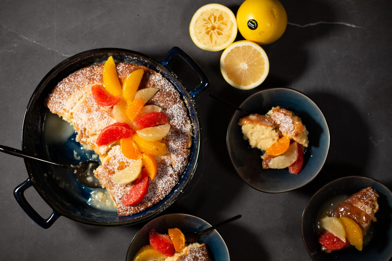 A citrus self-saucing pudding in a cast-iron pan with bowls served alongside, from above