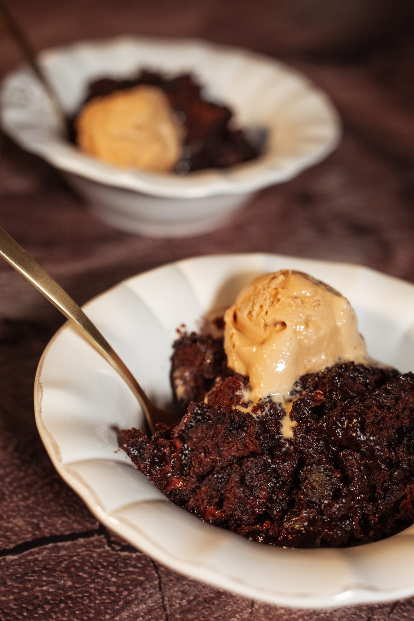 A bowl of chocolate pudding with ice cream and a gold spoon